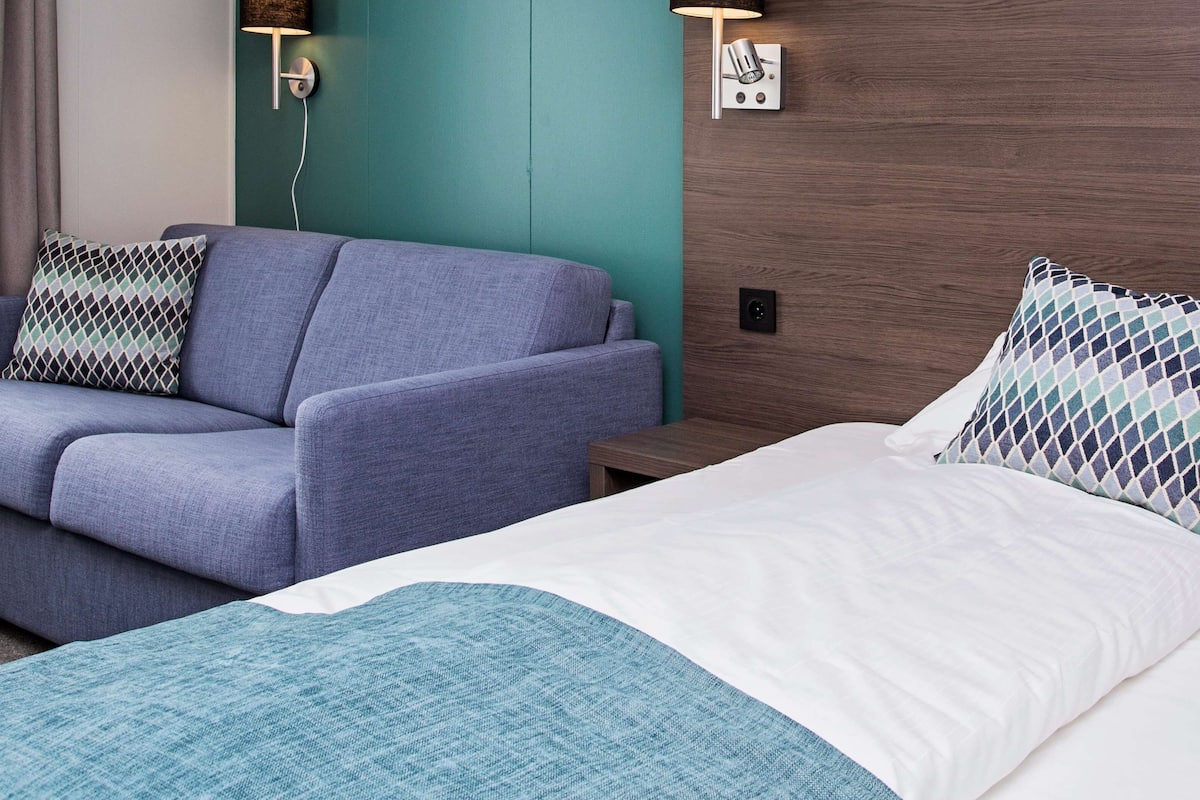 A hotel room with a blue sofa, a white bed, and a teal accent wall.