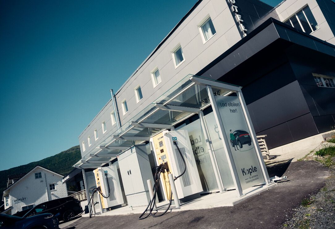 Un edificio moderno con fachada de vidrio, una estación de carga para autos y un letrero que dice "Koppel".