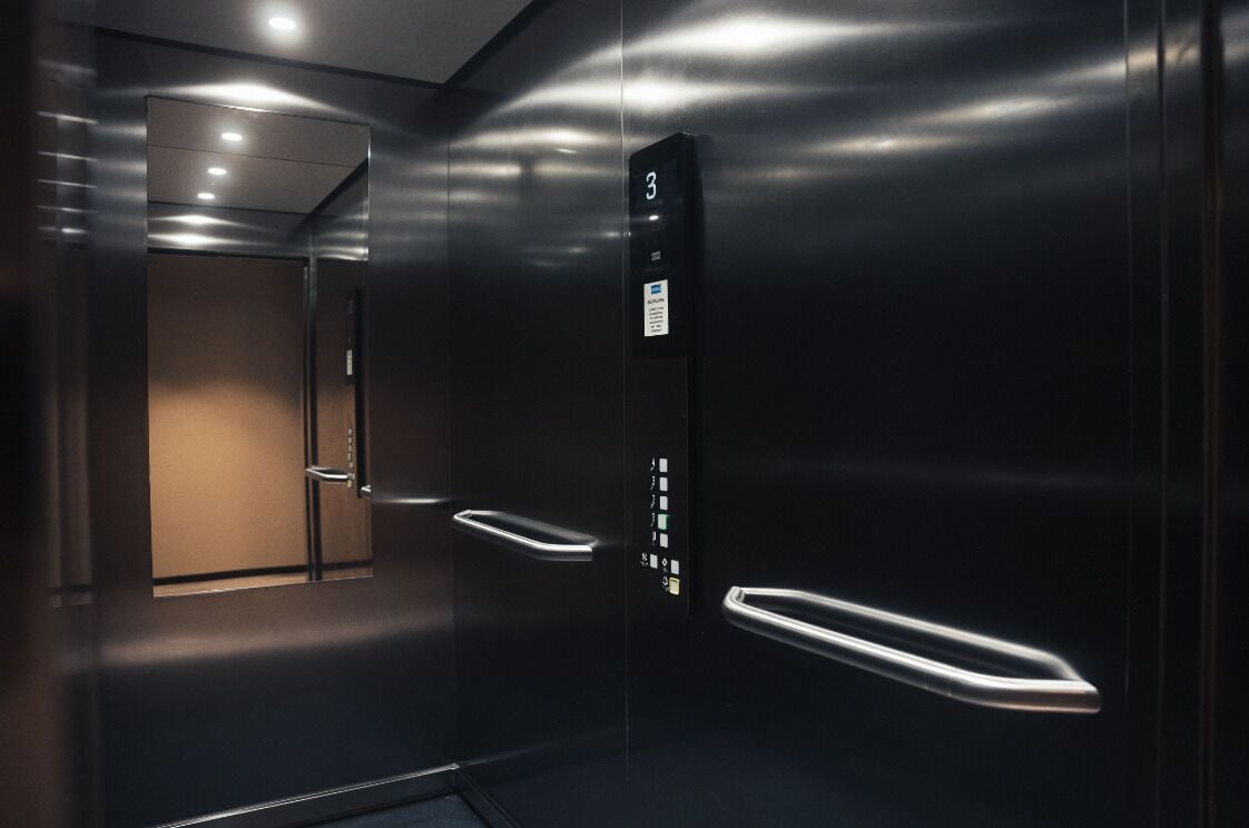 Un ascensor moderno con pantalla digital que muestra el número 3, interior metálico y puerta con manija.