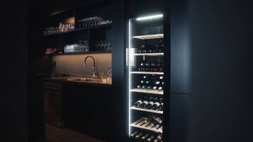 Una cocina moderna con nevera para vino integrada, un lavamanos y estantes llenos de botellas de vino.