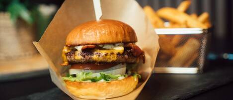 A burger in a paper container with fries in the background.