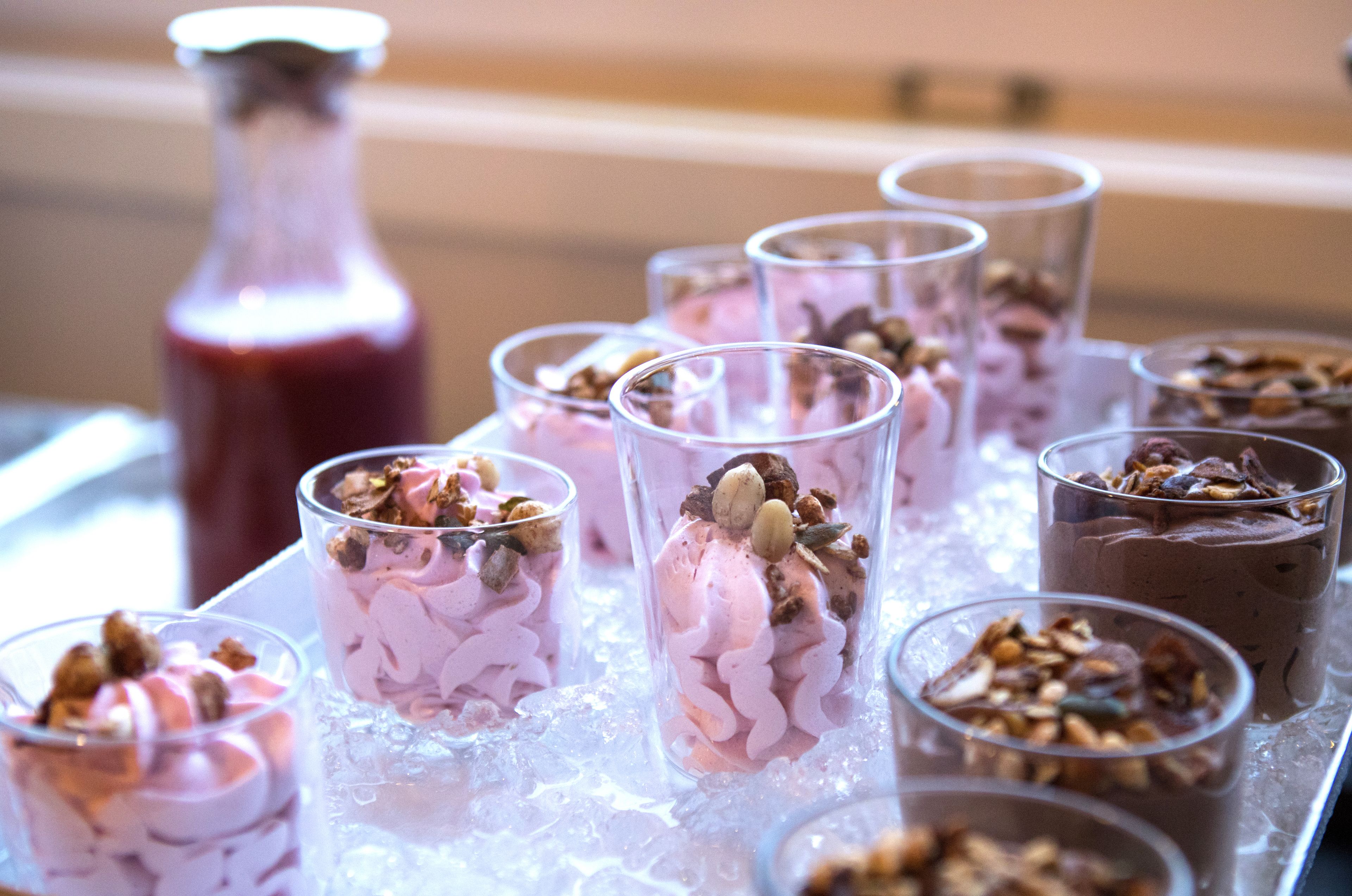 Una bandeja con copas de postre, hielo, cada una con un postre rosa cubierto de nueces y frutas secas.