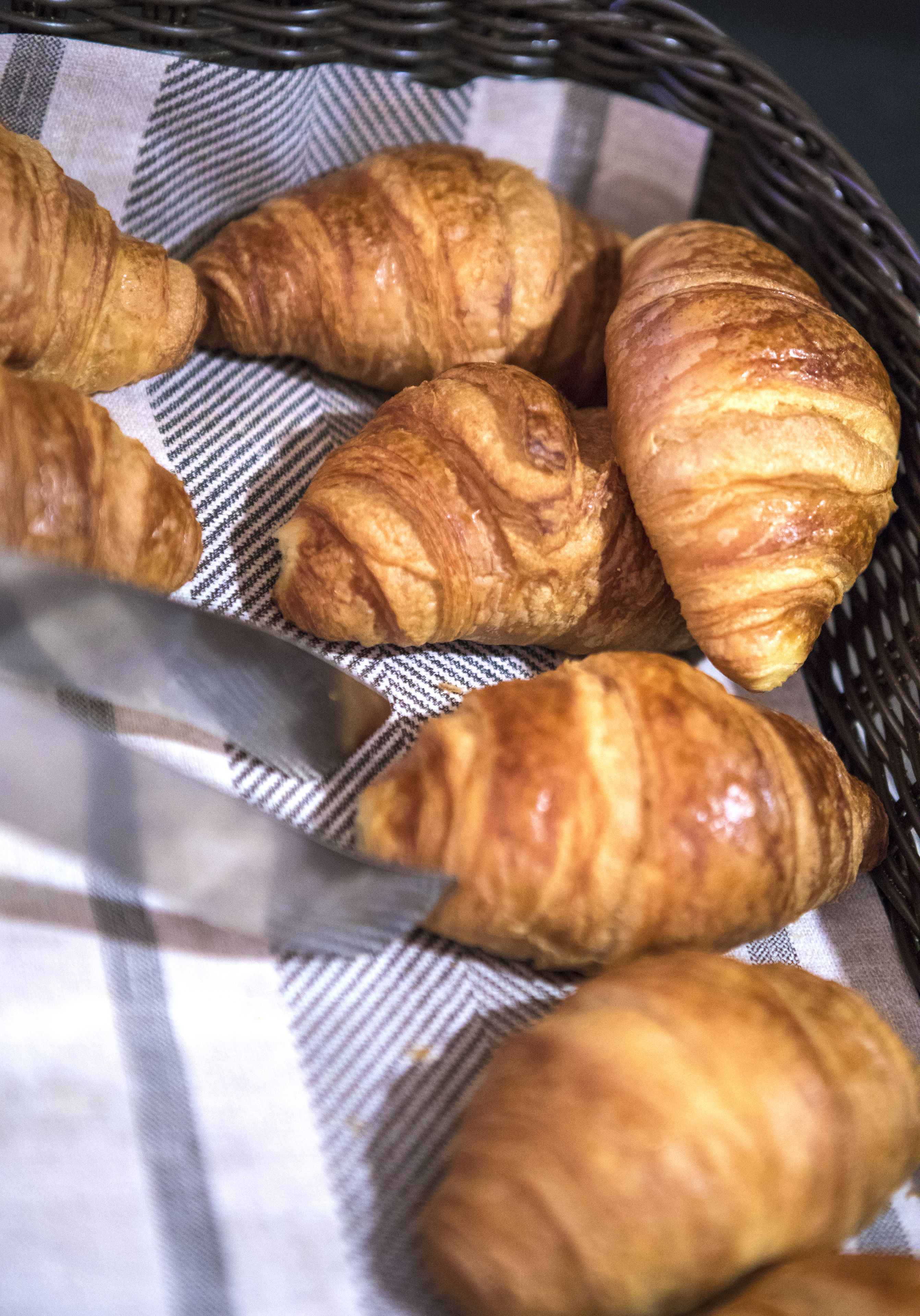 A basket of croissants on a checkered cloth.