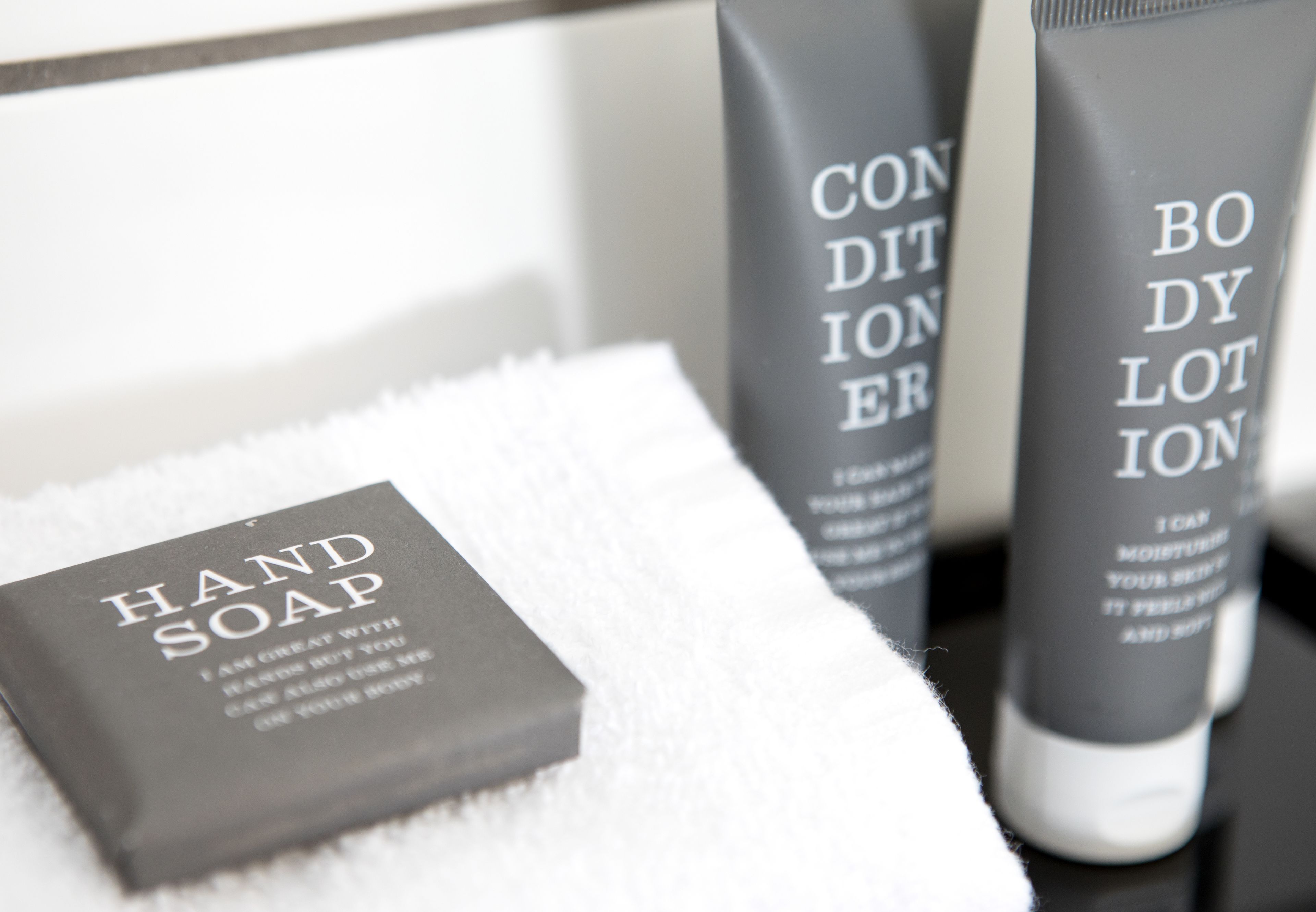 A set of toiletries including hand soap, conditioner, and lotion on a white towel.