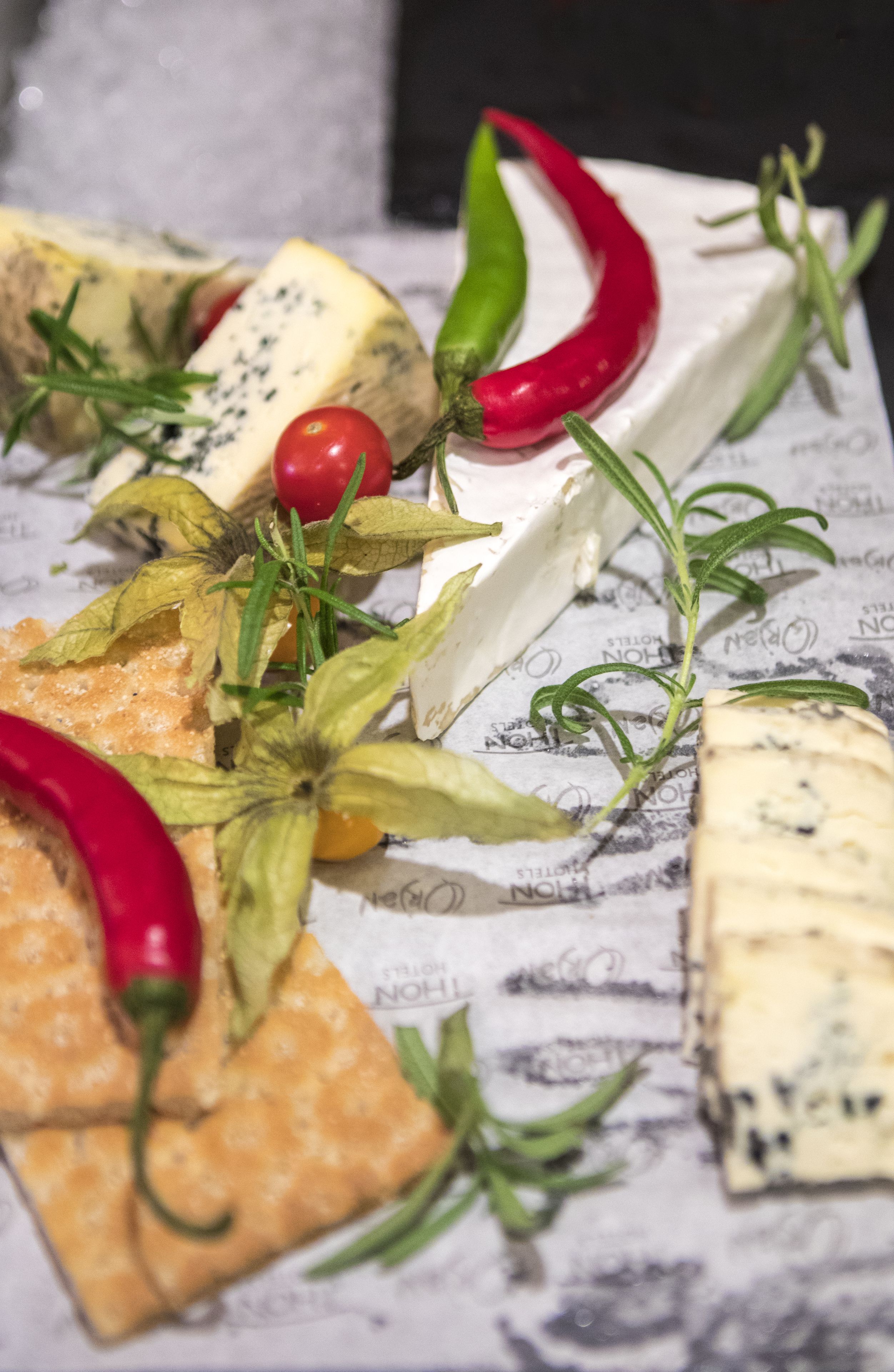 A cheese platter with various cheeses, crackers, and garnishes like red chili peppers and rosemary.