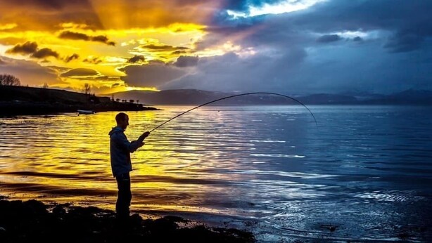 Une personne est en train de pêcher au bord d’un lac au coucher du soleil.