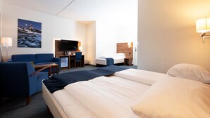 Une chambre d’hôtel comprenant un lit, un bureau avec un ordinateur, une télévision et un coin salon avec des fauteuils.