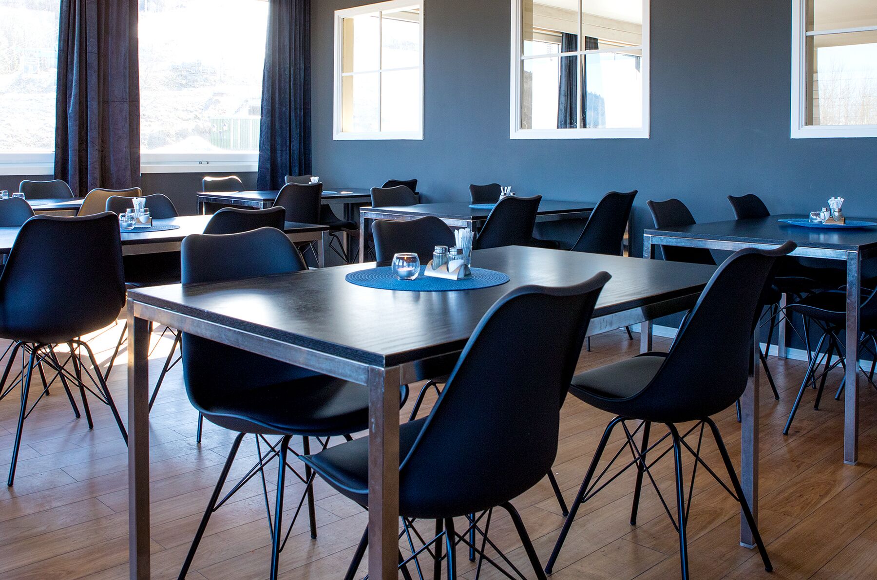 A modern dining area with multiple tables and chairs, large windows, and a view of the outside.