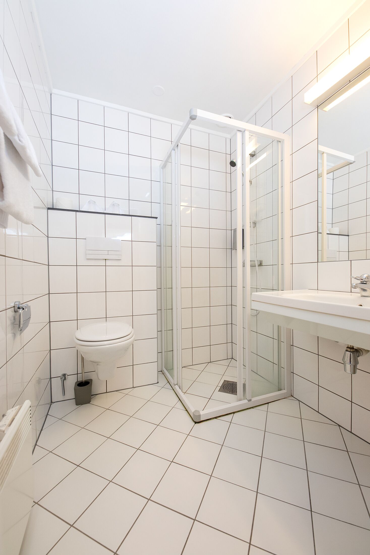 Een moderne badkamer met witte tegels, een douche met glazen wand, een wastafel en een toilet.