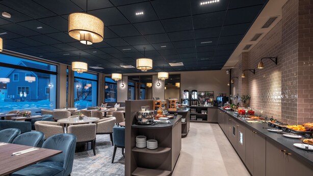 A modern hotel dining area with round tables, blue chairs, a buffet counter, and a brick wall. - Thon Hotel Andrikken (Andoy)
