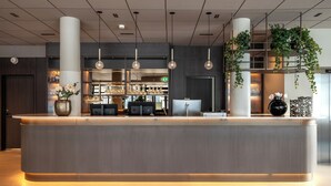 A reception desk with a modern design, overhead lighting, and a visible bar area in the background. - Thon Hotel Andrikken (Andoy)