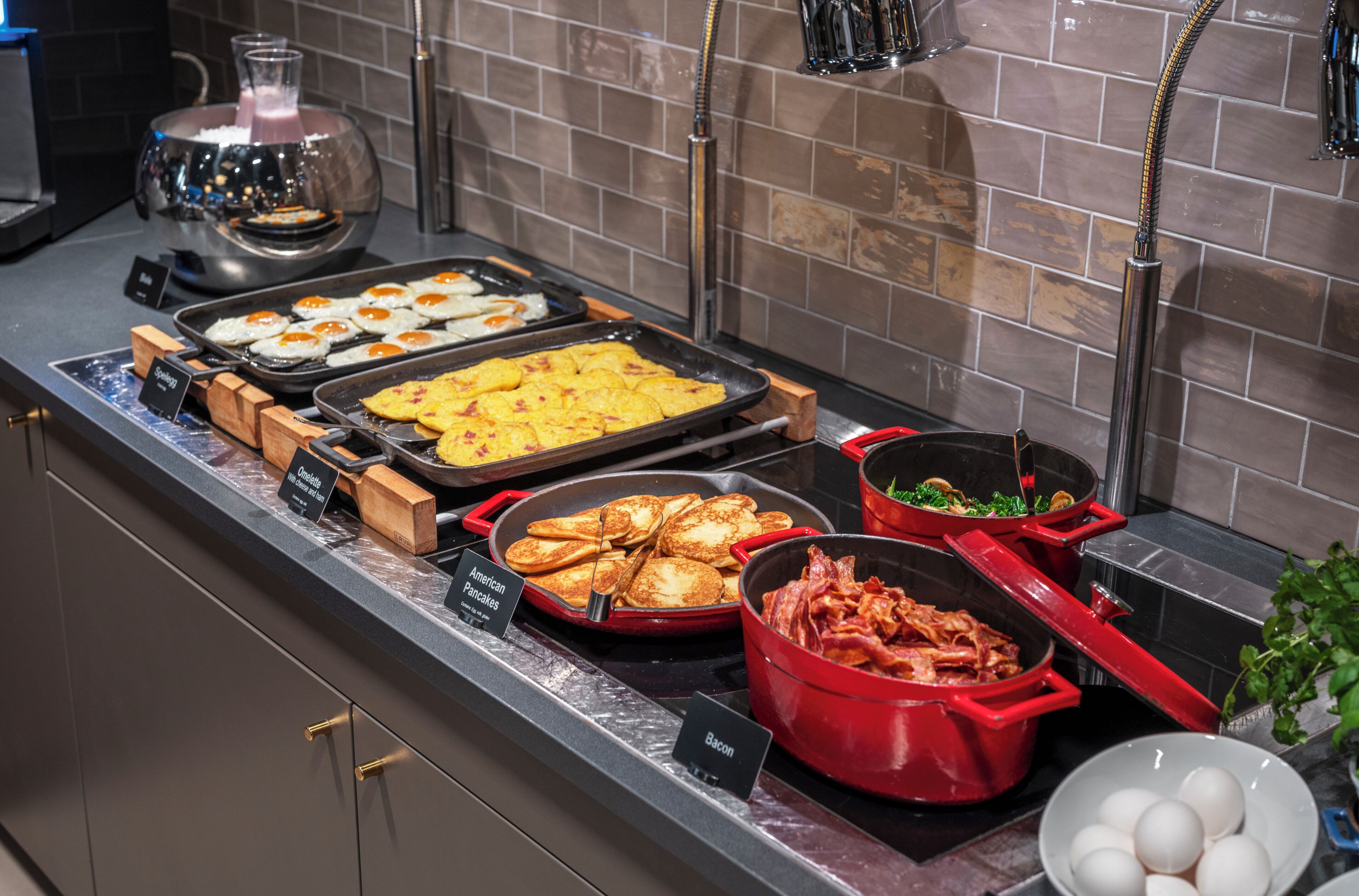 Un bufé con diversas opciones de comida, incluyendo huevos, panqueques y tocino.
