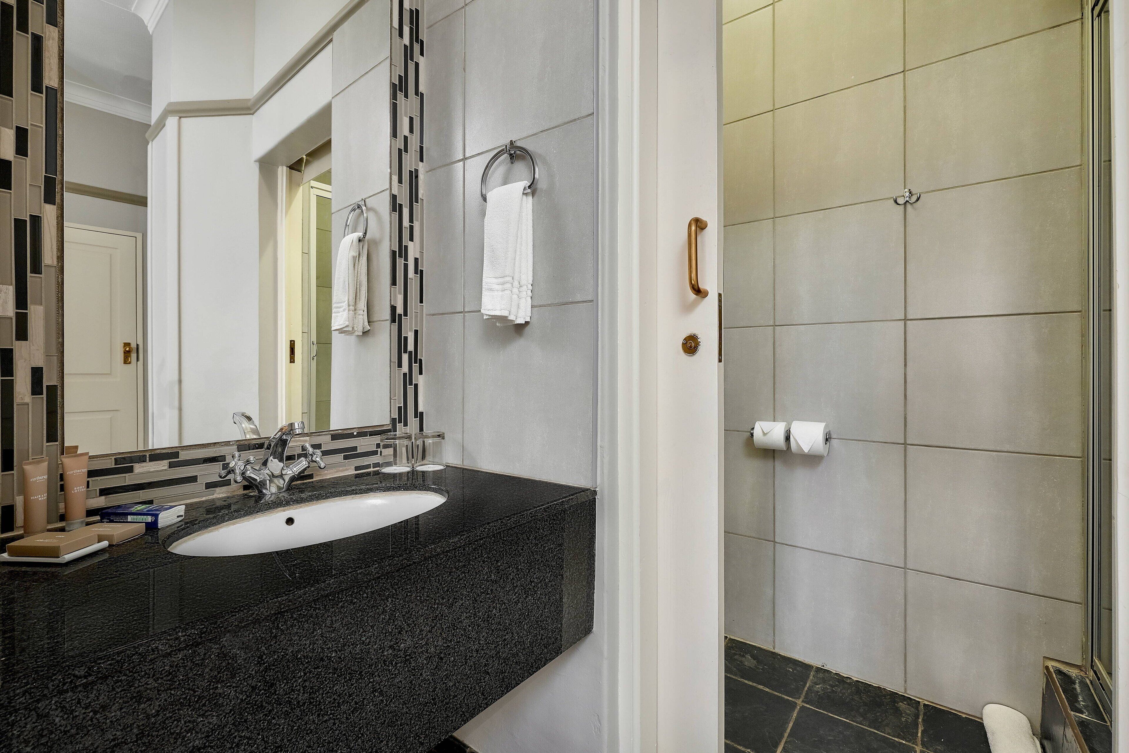 A modern bathroom with a black granite sink, a large mirror, and a shower area with tiled walls.