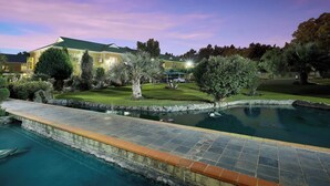 Uma casa grande com piscina, cercada por um gramado bem cuidado e árvores.
