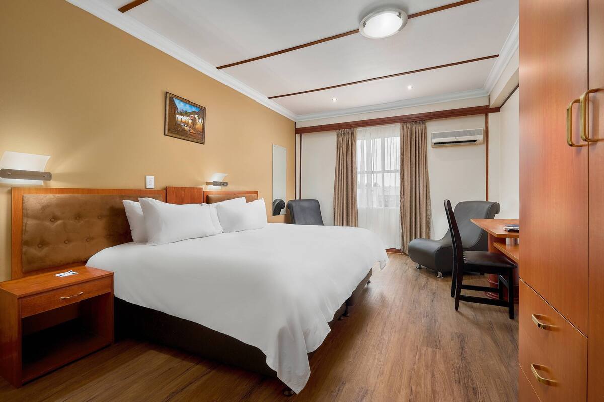 Une chambre d’hôtel avec un grand lit, des tables de chevet, un bureau et une armoire.