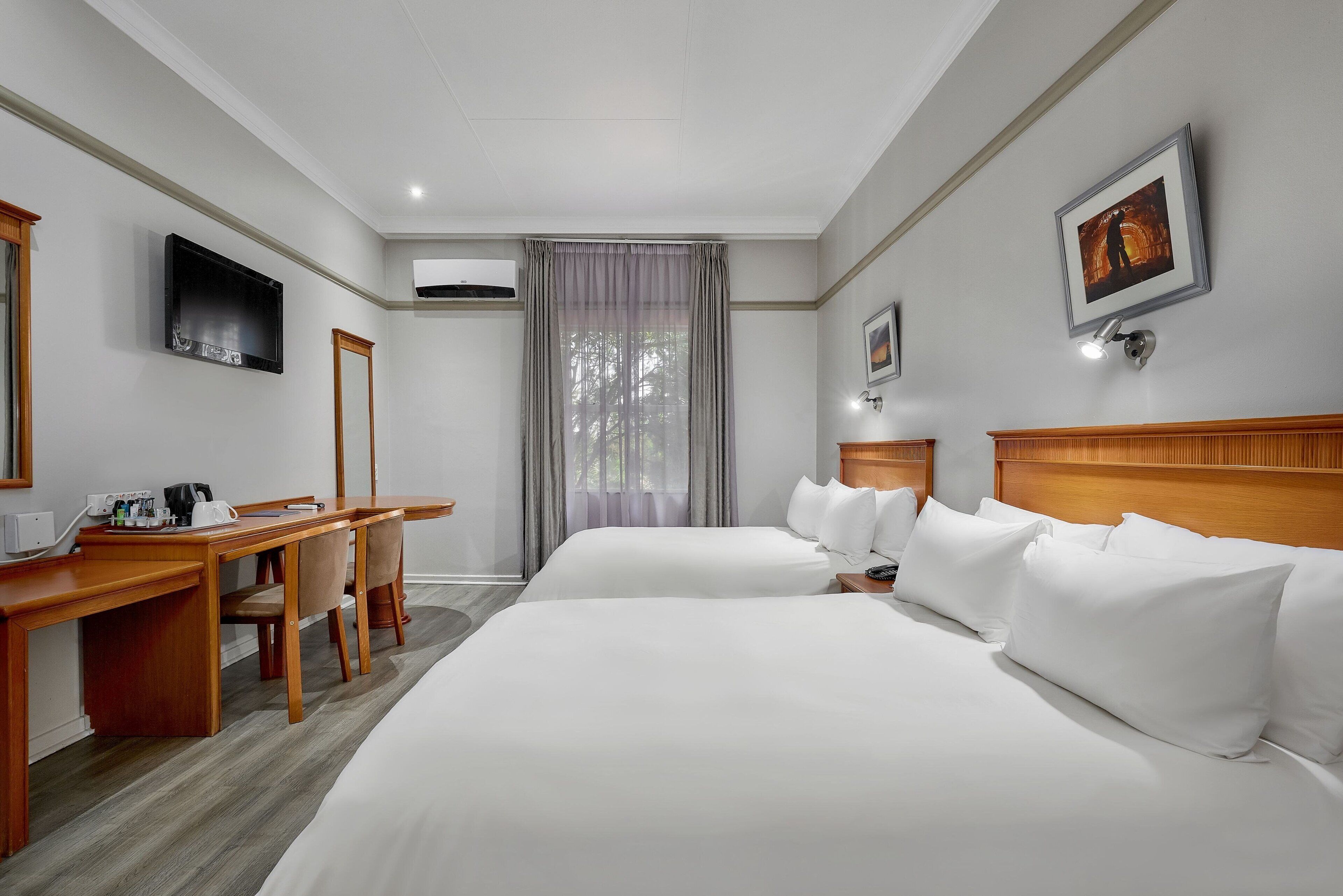 A hotel room with two beds, a desk, a chair, a TV, and a window with curtains.