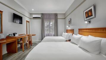 A hotel room with two beds, a desk, a chair, a TV, and a window with curtains.