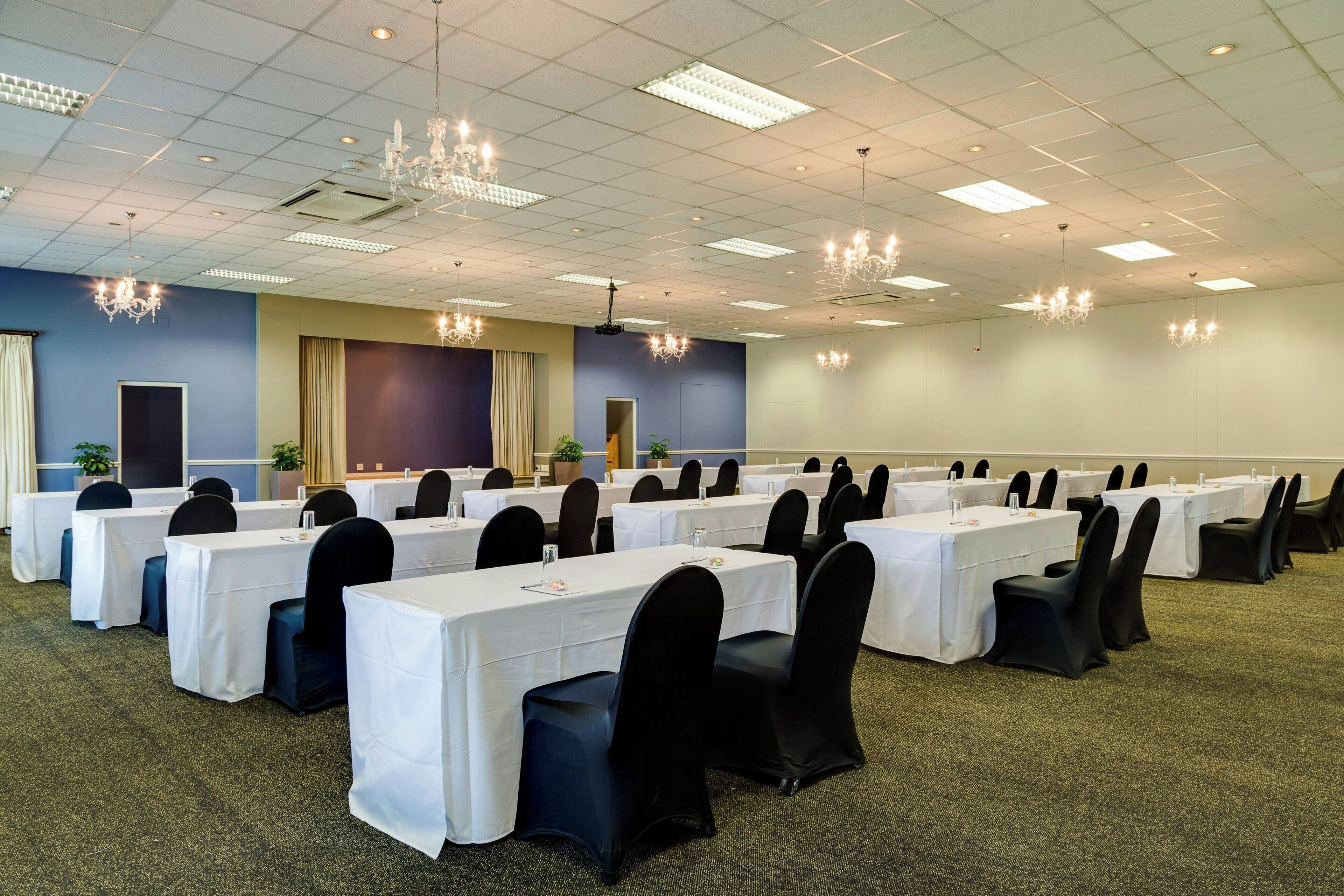 Un salón de conferencias con varias mesas y sillas, un candelabro y suelo alfombrado.
