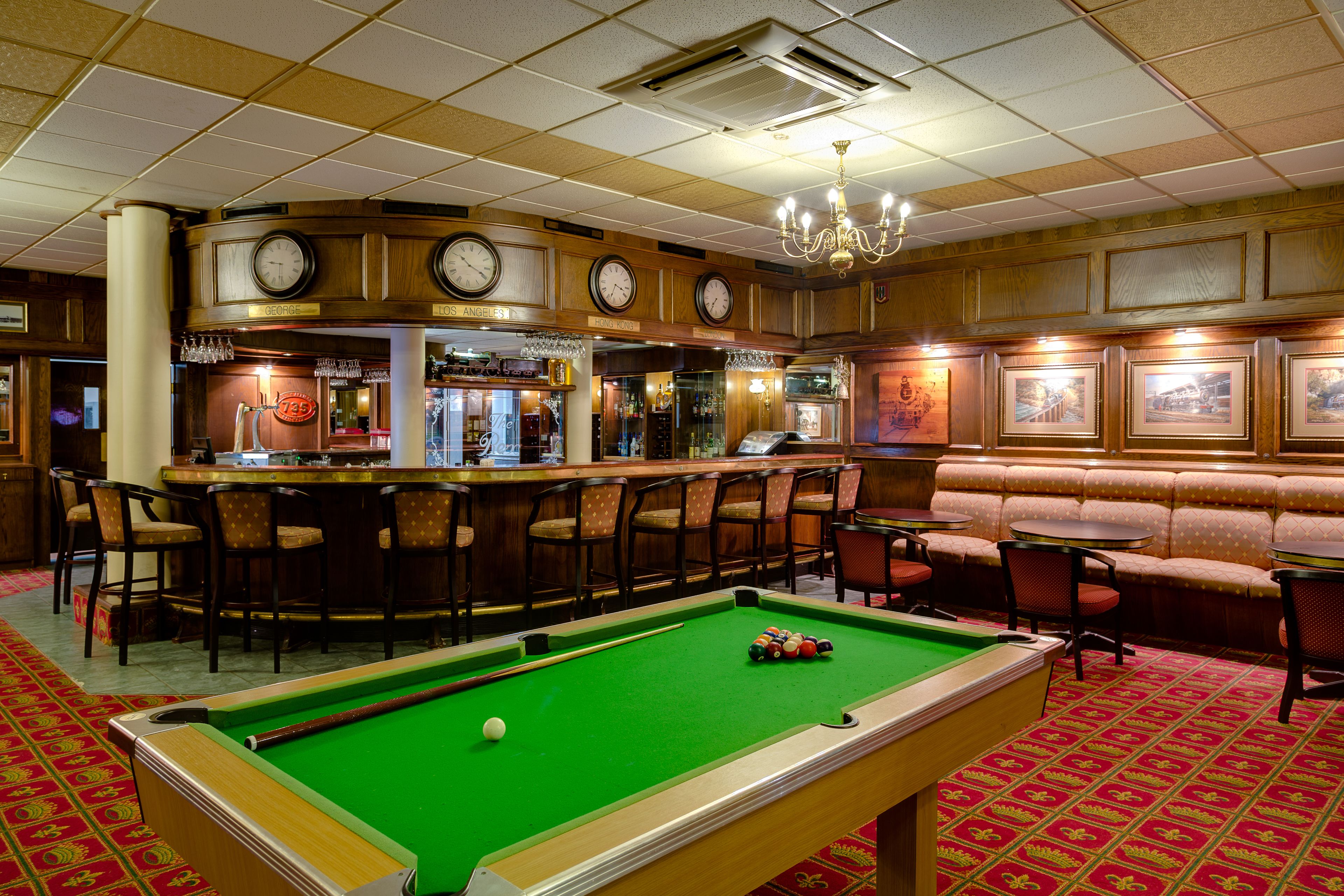 A pool table with a green felt surface, a bar area with stools, and a seating area with cushioned benches.
