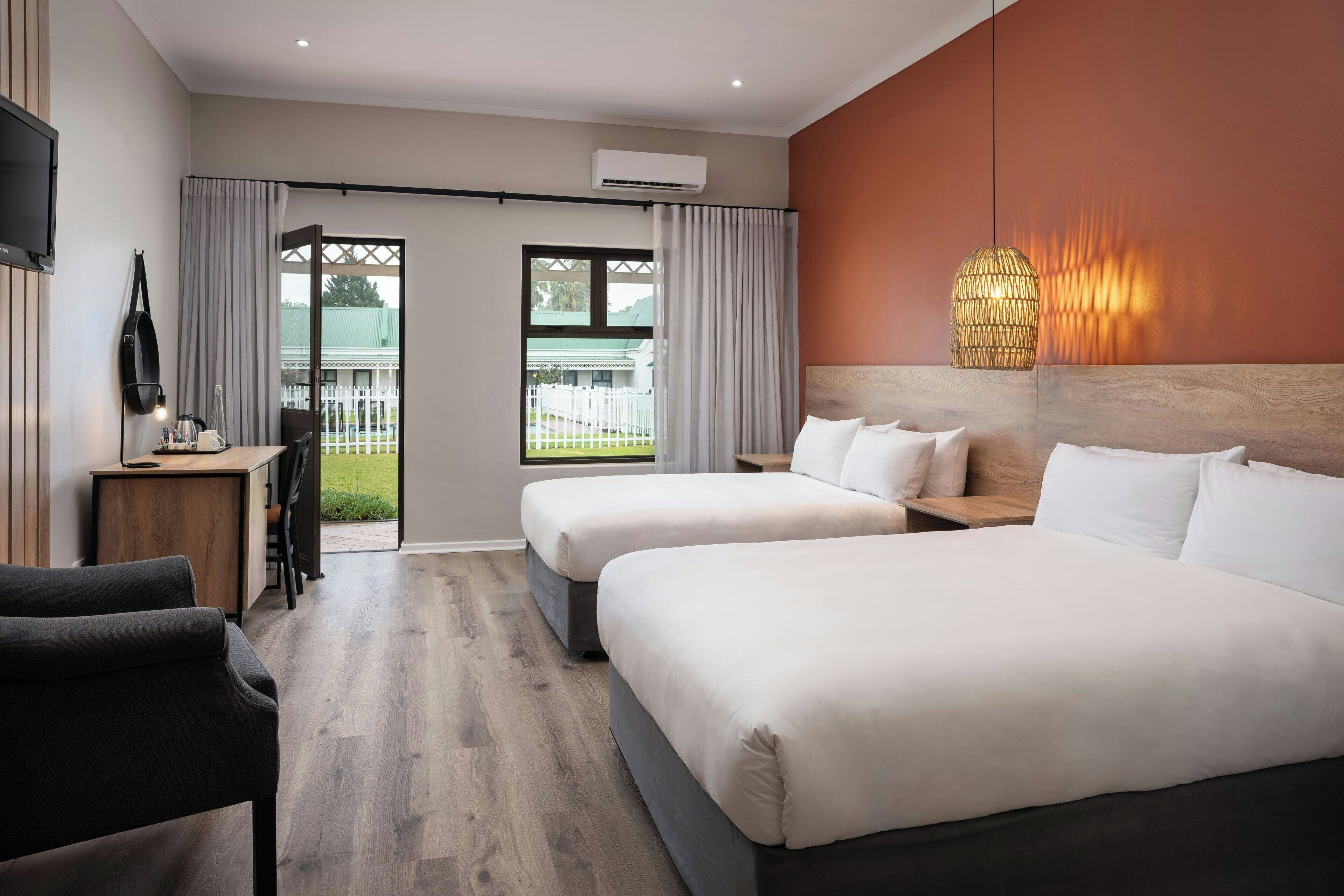 A hotel room with two beds, a desk, a chair, and a large window with curtains.