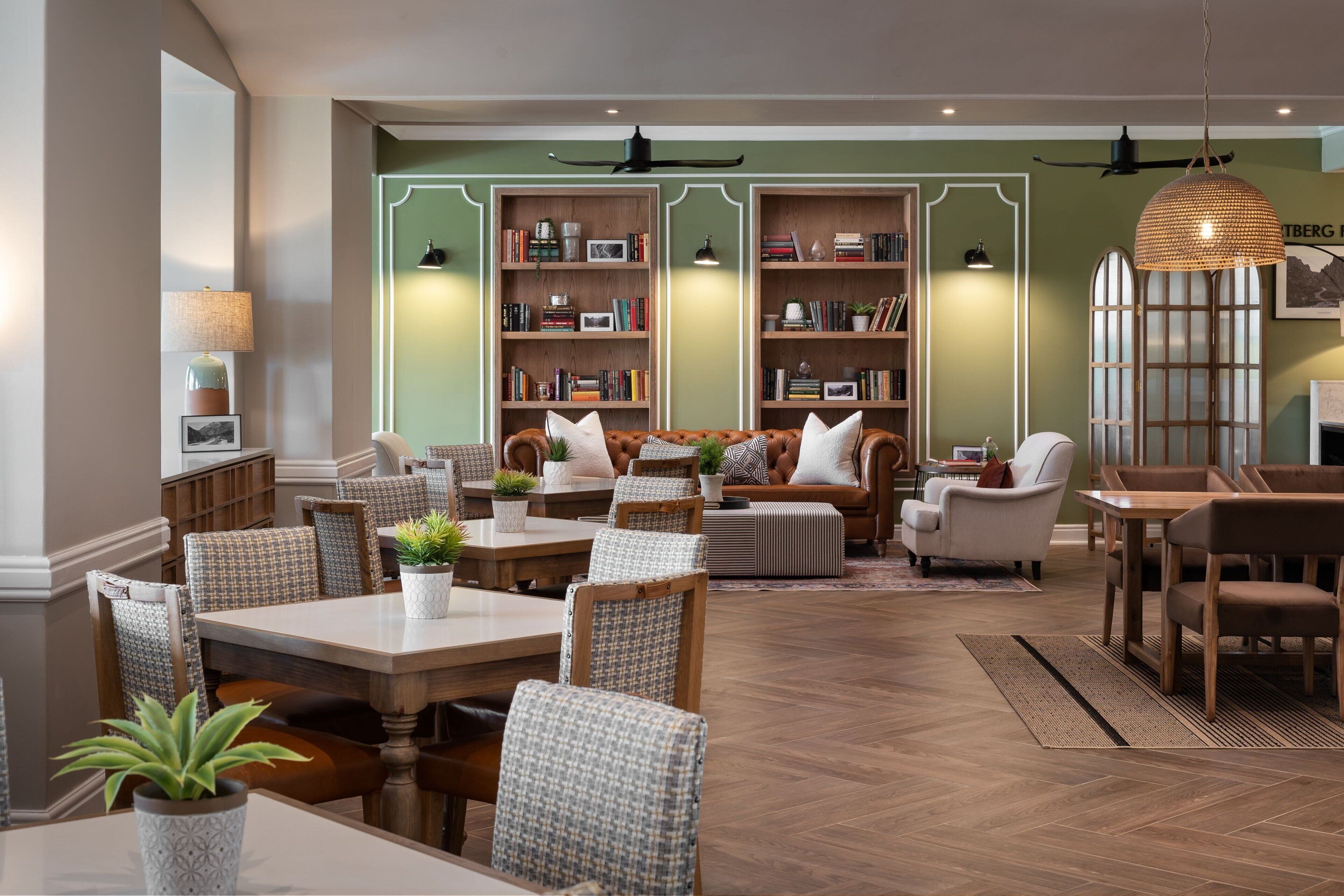 Amplia sala de estar con un sofá grande, varias sillas, una mesa de comedor y dos estanterías llenas de libros y objetos decorativos.