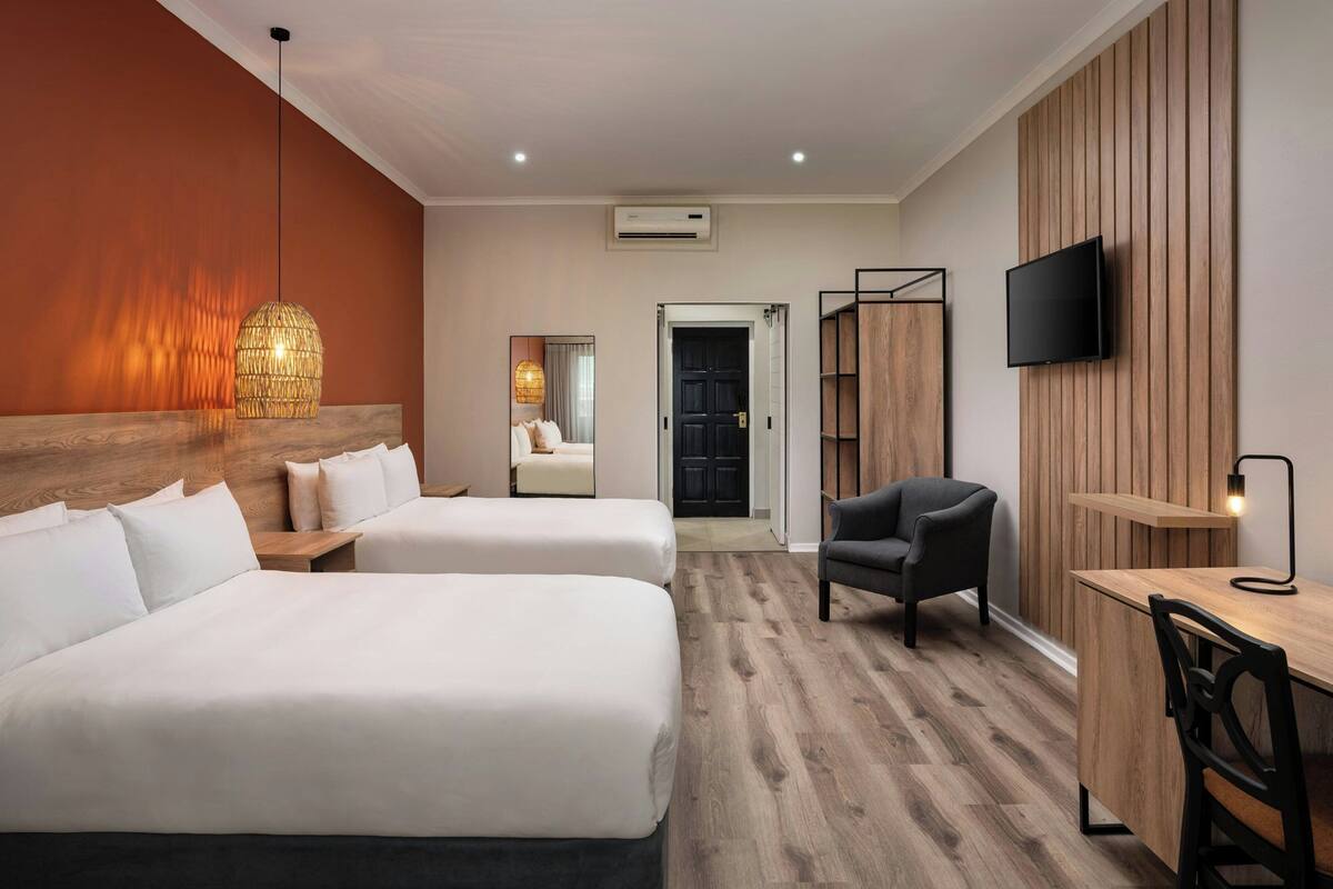 A hotel room with two beds, a desk, a chair, a TV, and a wooden panel wall.
