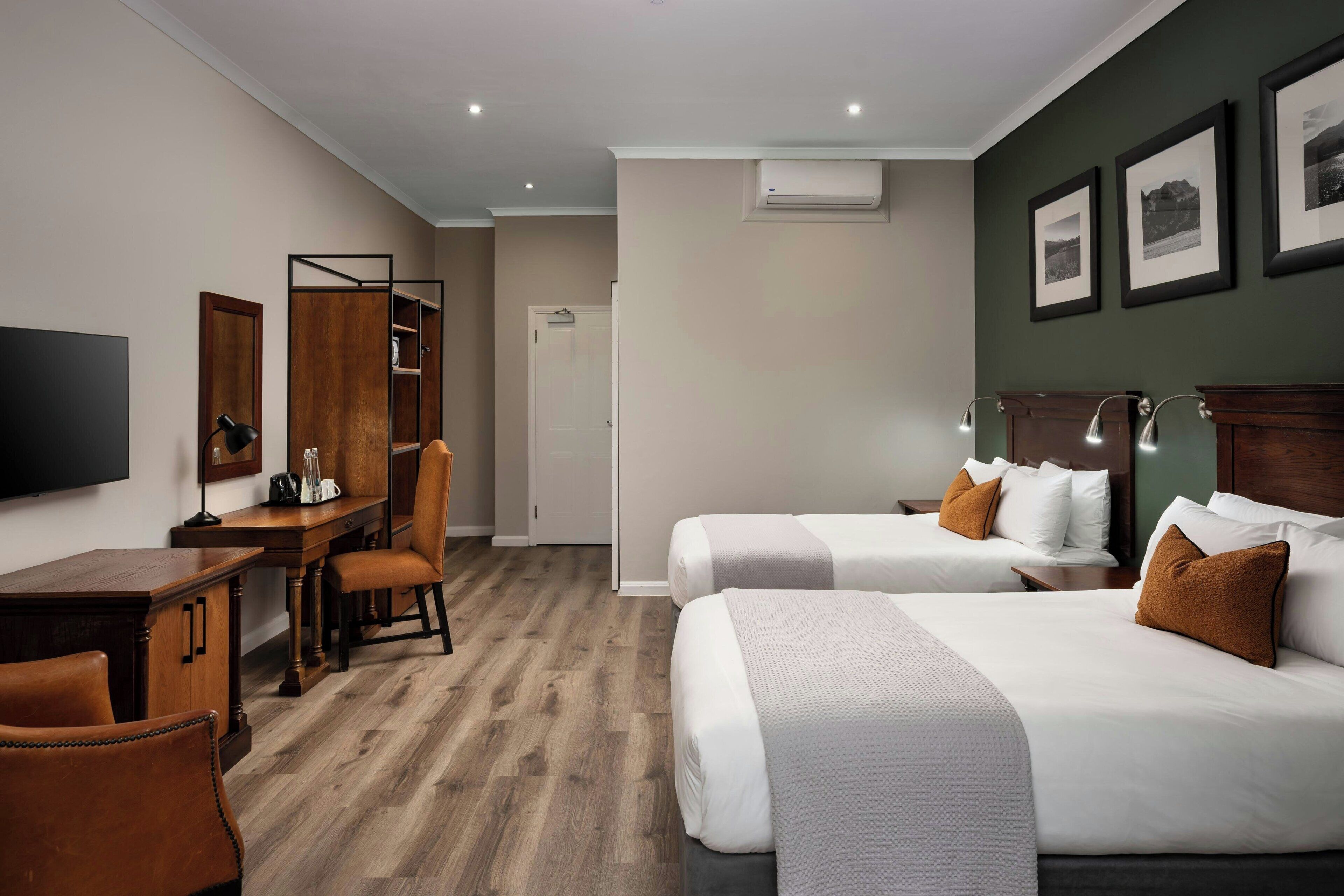 Een hotelkamer met twee bedden, een bureau, een stoel, een televisie en ingelijste foto's aan de muur.
