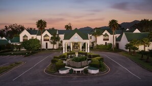 A hotel with a symmetrical facade, a central entrance, and a landscaped garden with neatly trimmed bushes and a fountain. - Protea Hotel by Marriott George King George (George)