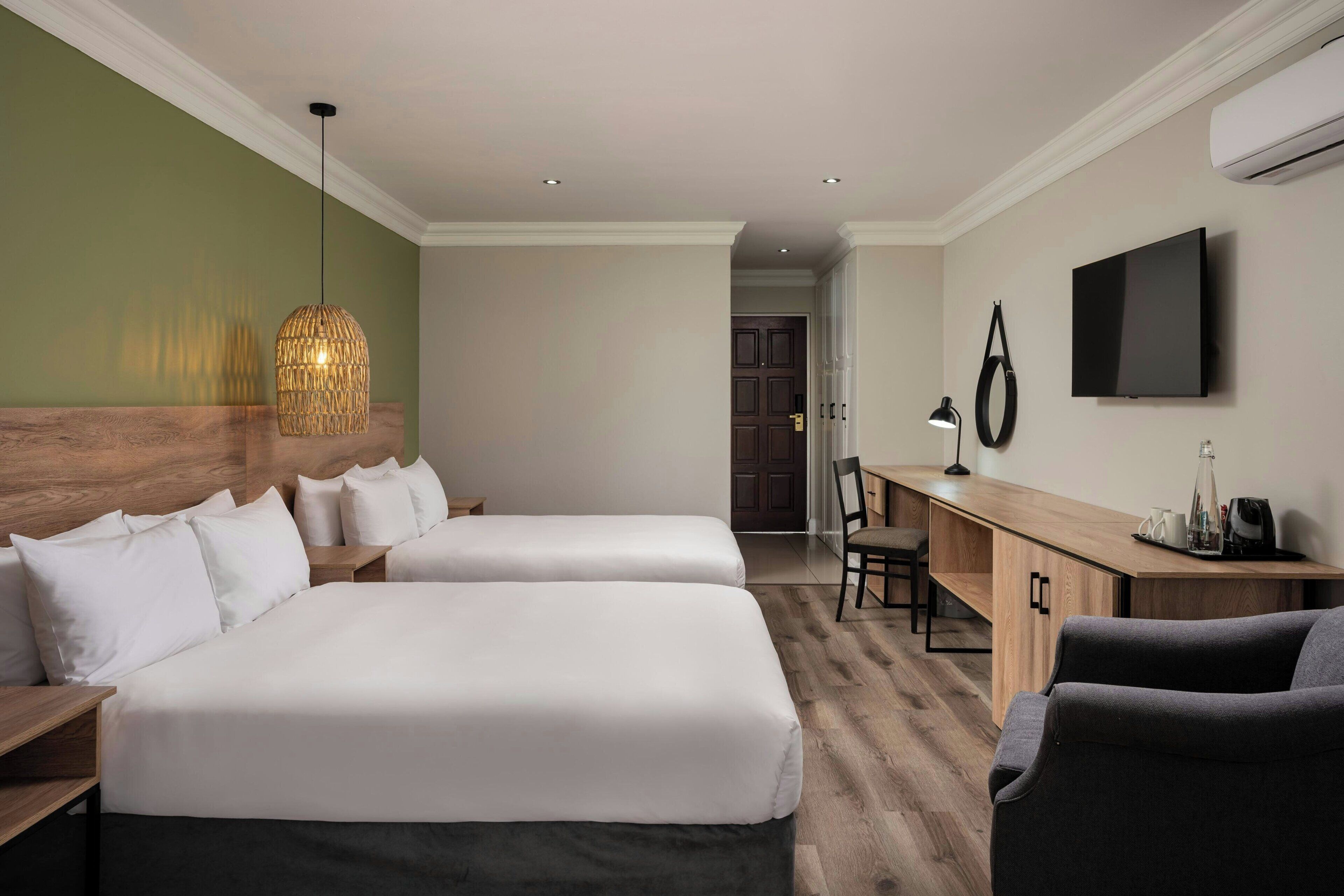 A hotel room with two beds, a desk, a chair, a TV, and a hanging light fixture.