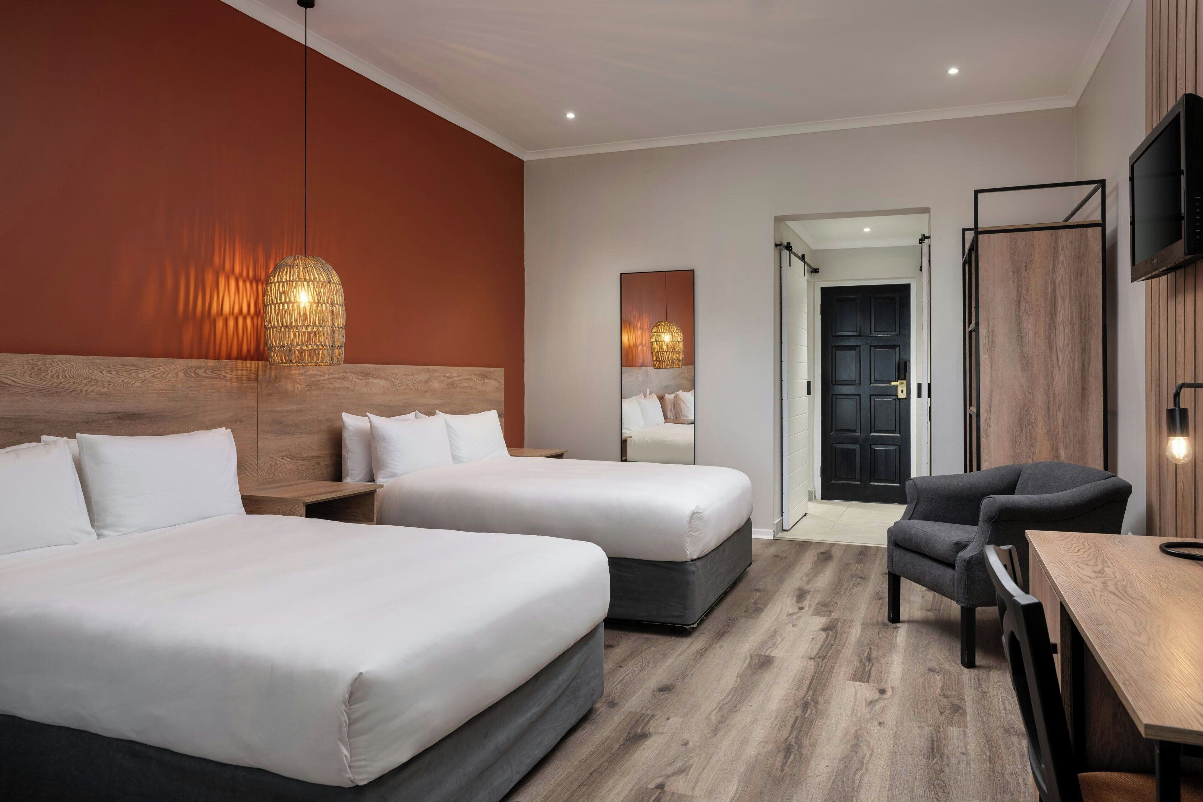 Ett hotellrum med två sängar, en sänggavel i trä, en TV och en matplats.