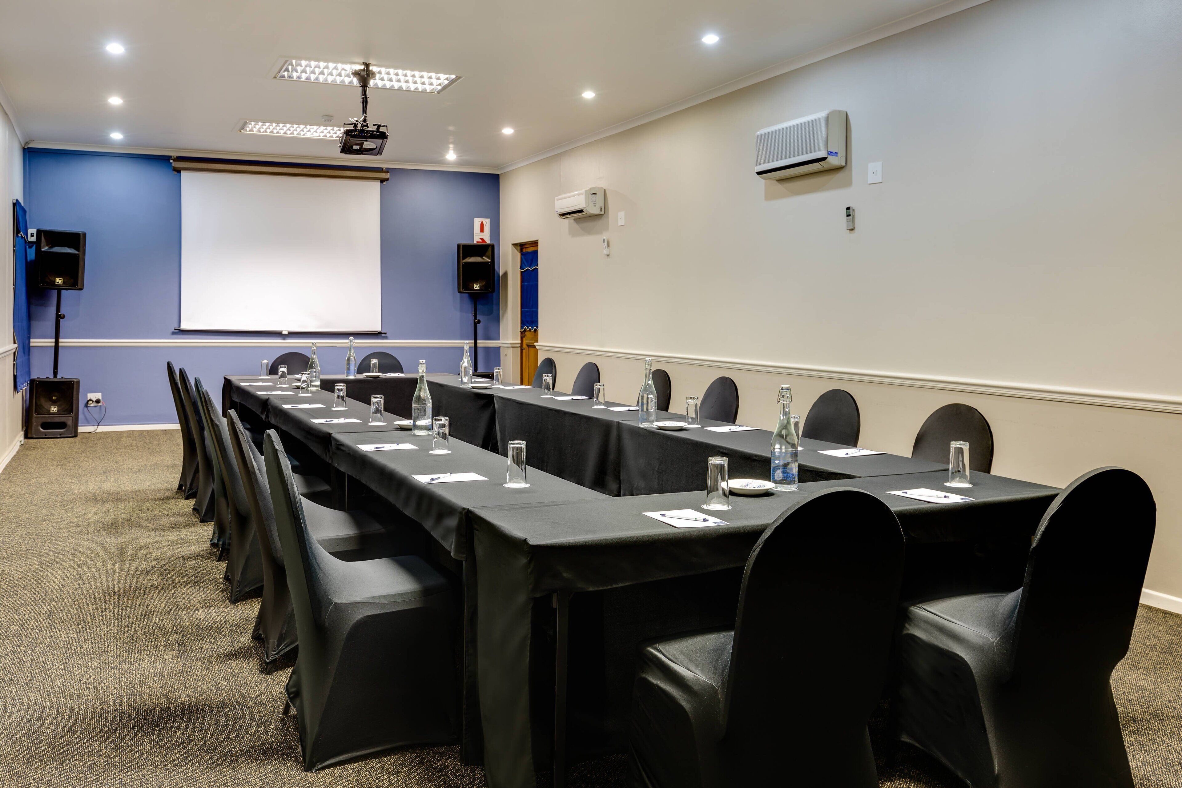 Une salle de conférence équipée d’une longue table, de chaises, d’un écran de projection et d’un appareil de climatisation.