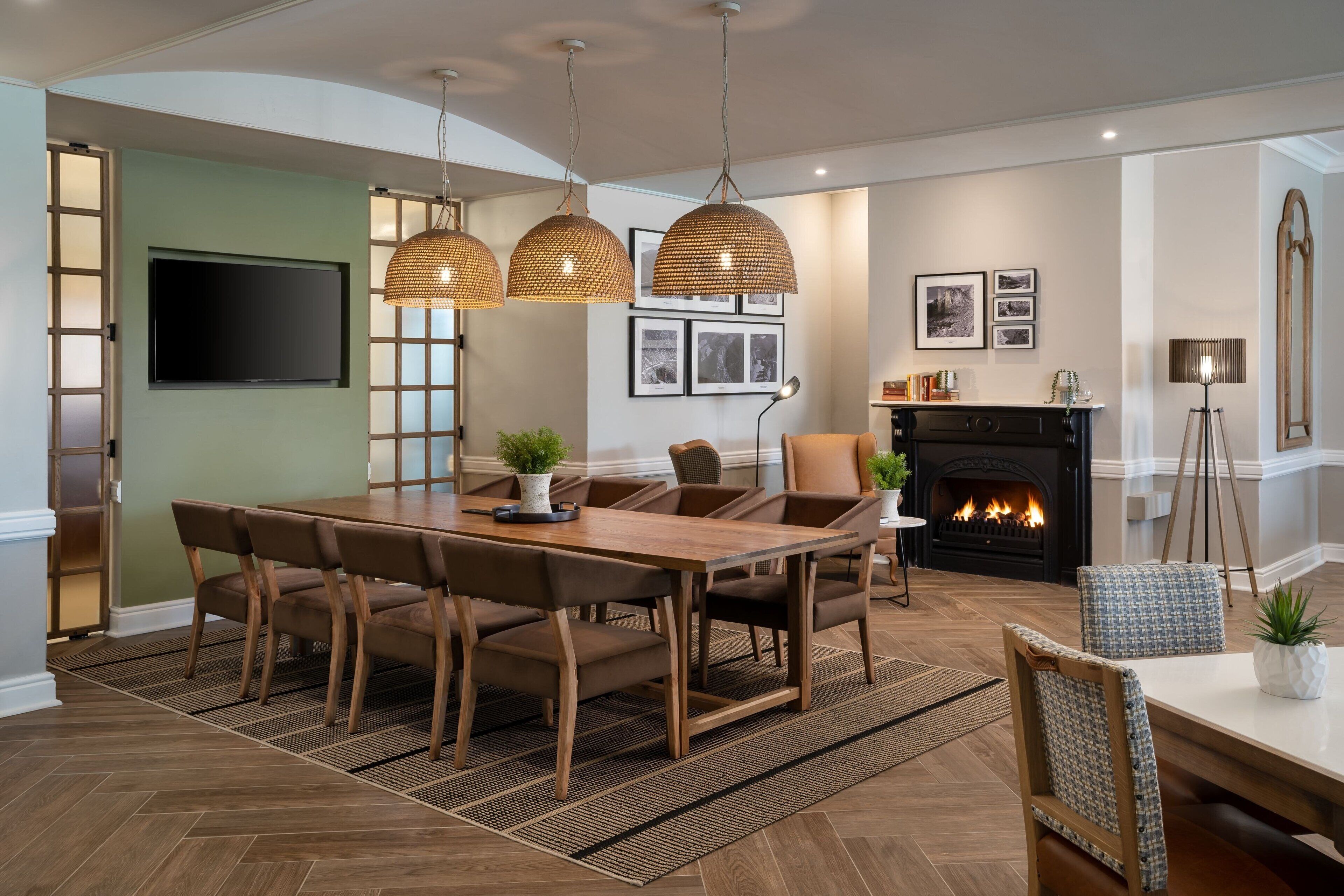 A dining area with a wooden table and chairs, a fireplace, and hanging pendant lights.