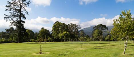 Un campo de golf con cielo despejado, árboles y una cadena montañosa a lo lejos.
