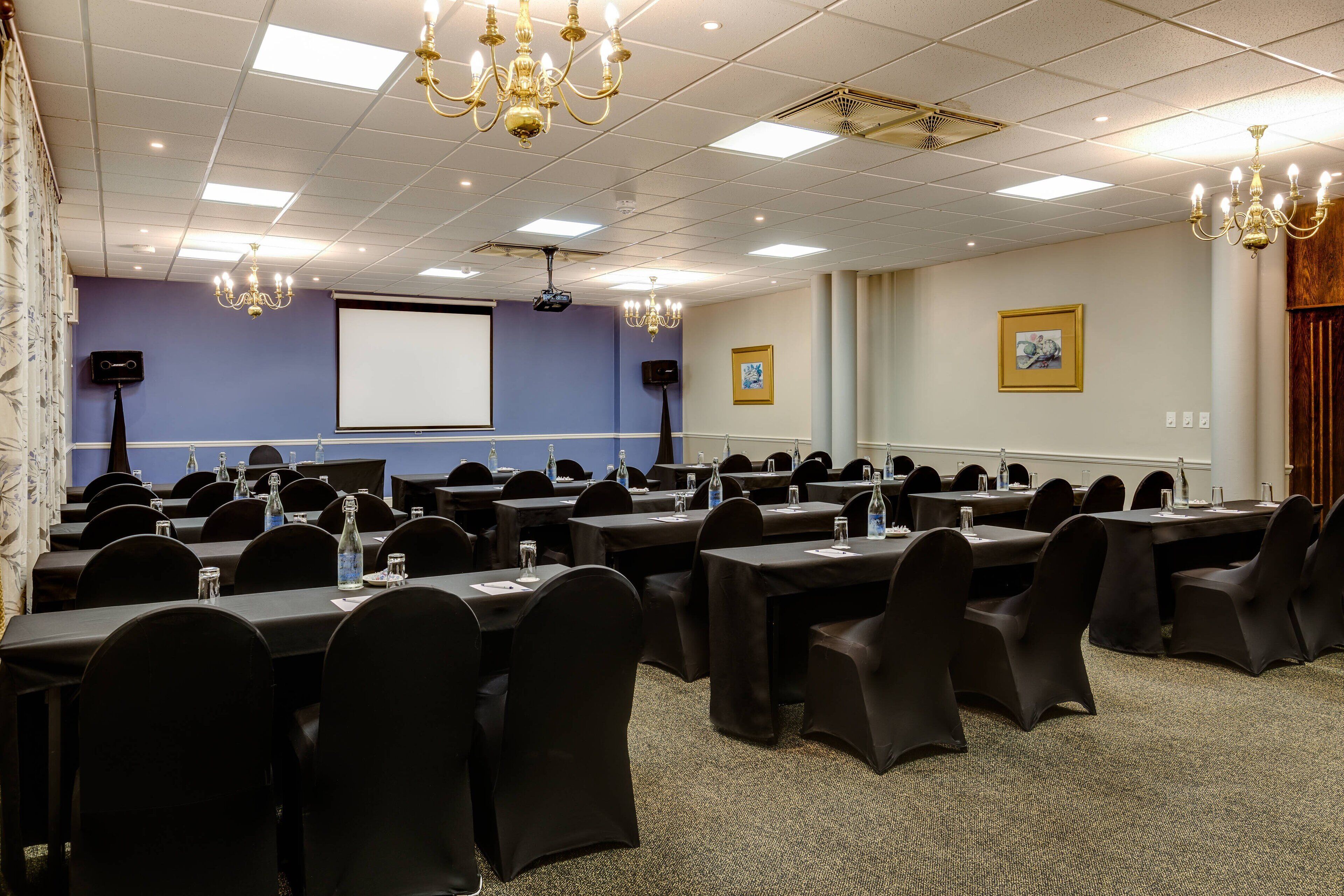 A conference room with multiple tables and chairs, a projector screen, and a large window with curtains.
