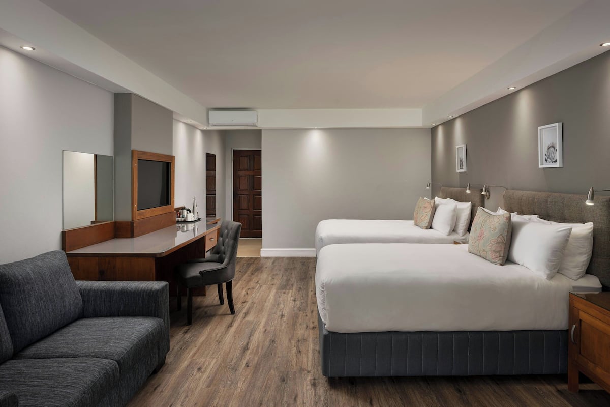 A modern hotel room with a large bed, a desk, a chair, and a sofa.
