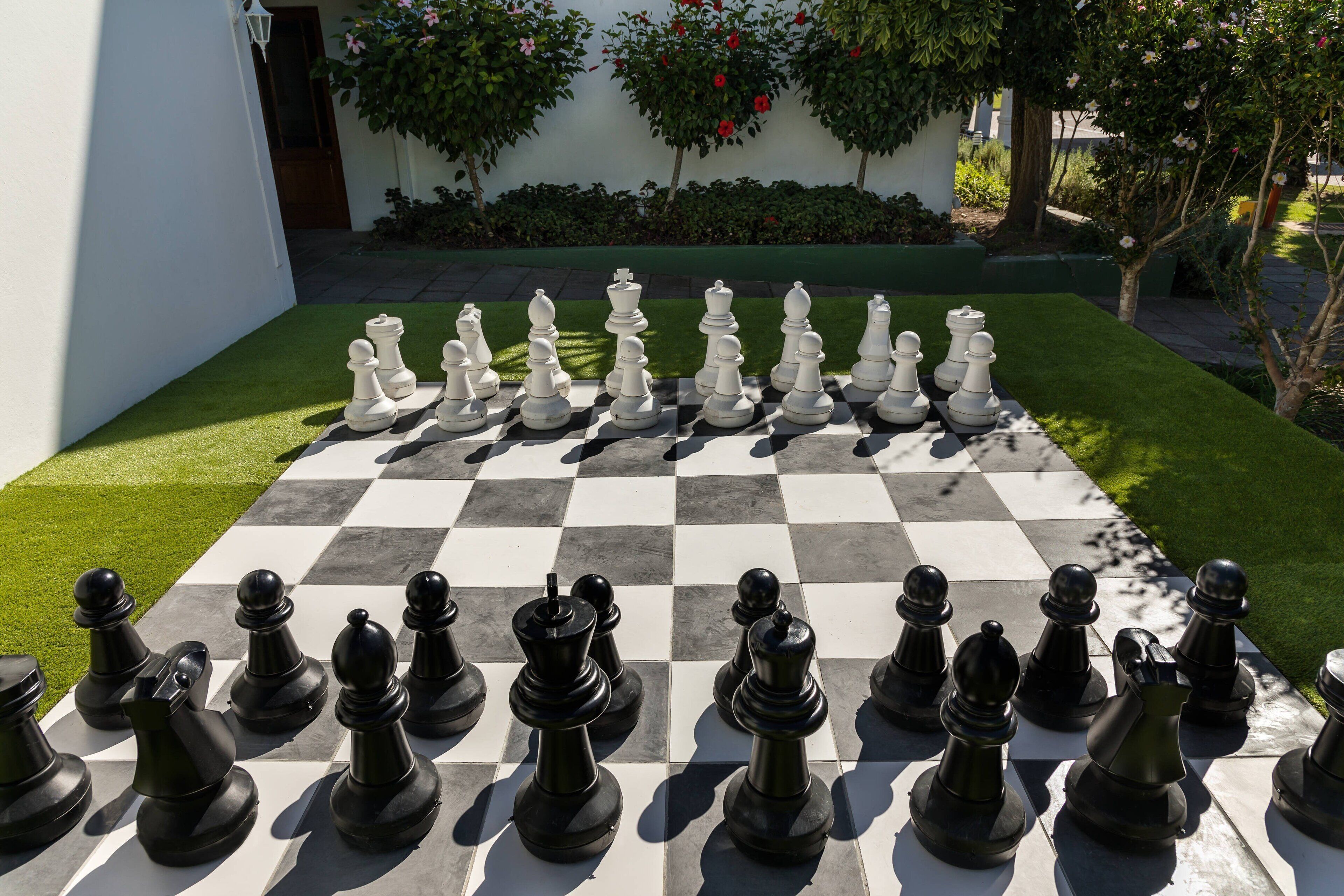 A chessboard set up outdoors with a white building in the background.