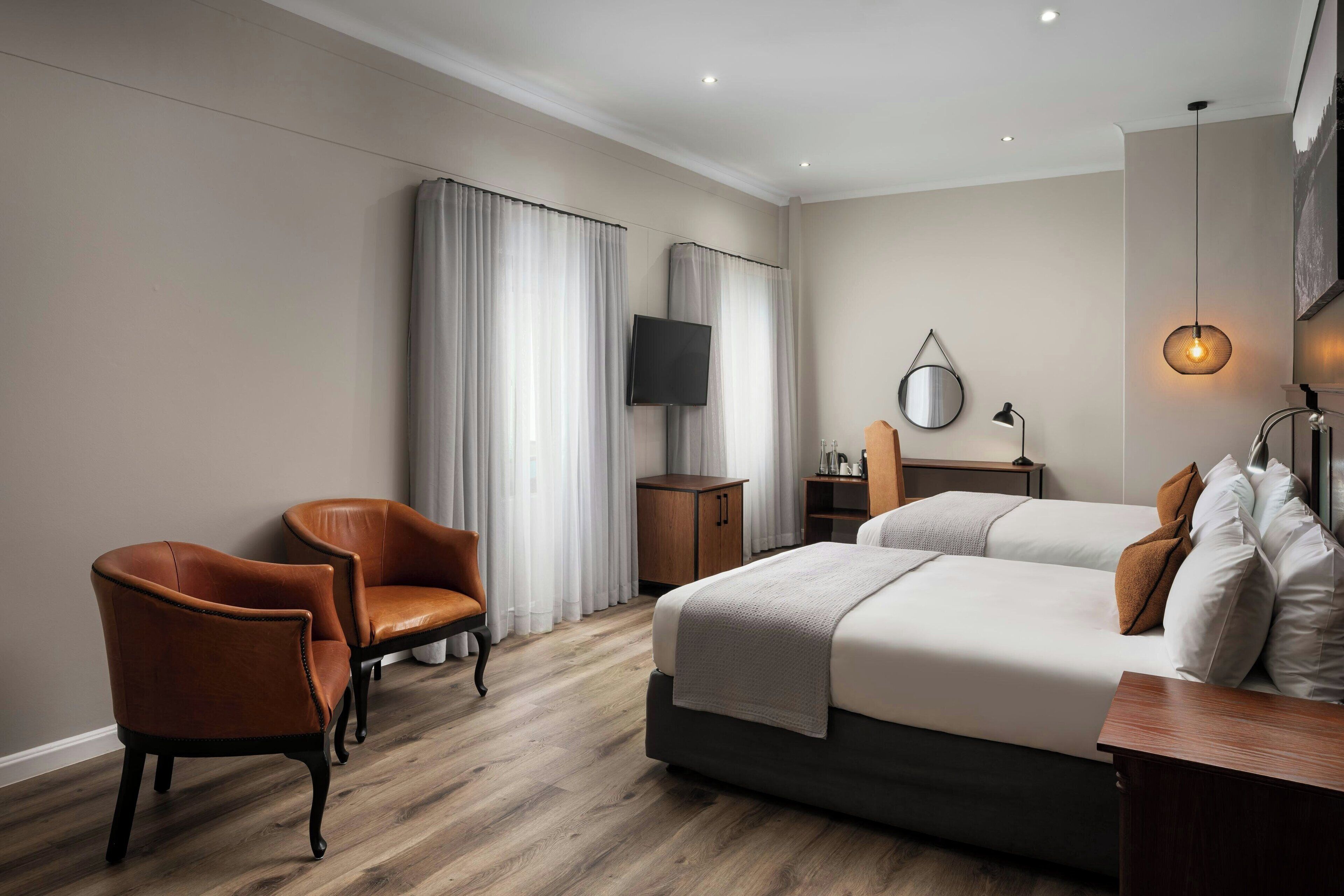A hotel room with a bed, two chairs, a TV, a desk, and a lamp.