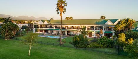 Un hotel con piscina, césped verde y palmeras.