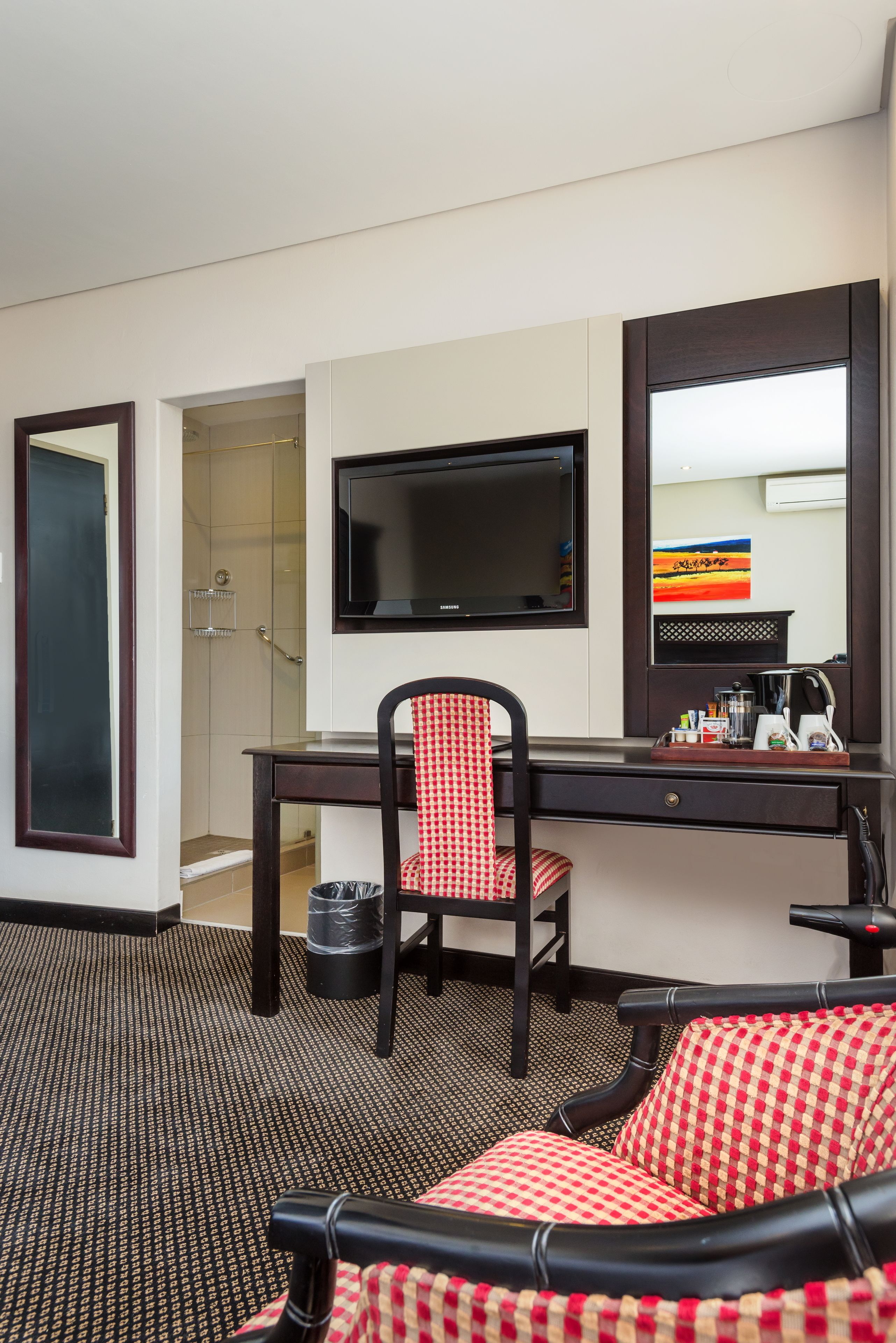 A hotel room with a desk, chair, television, and a shower area.