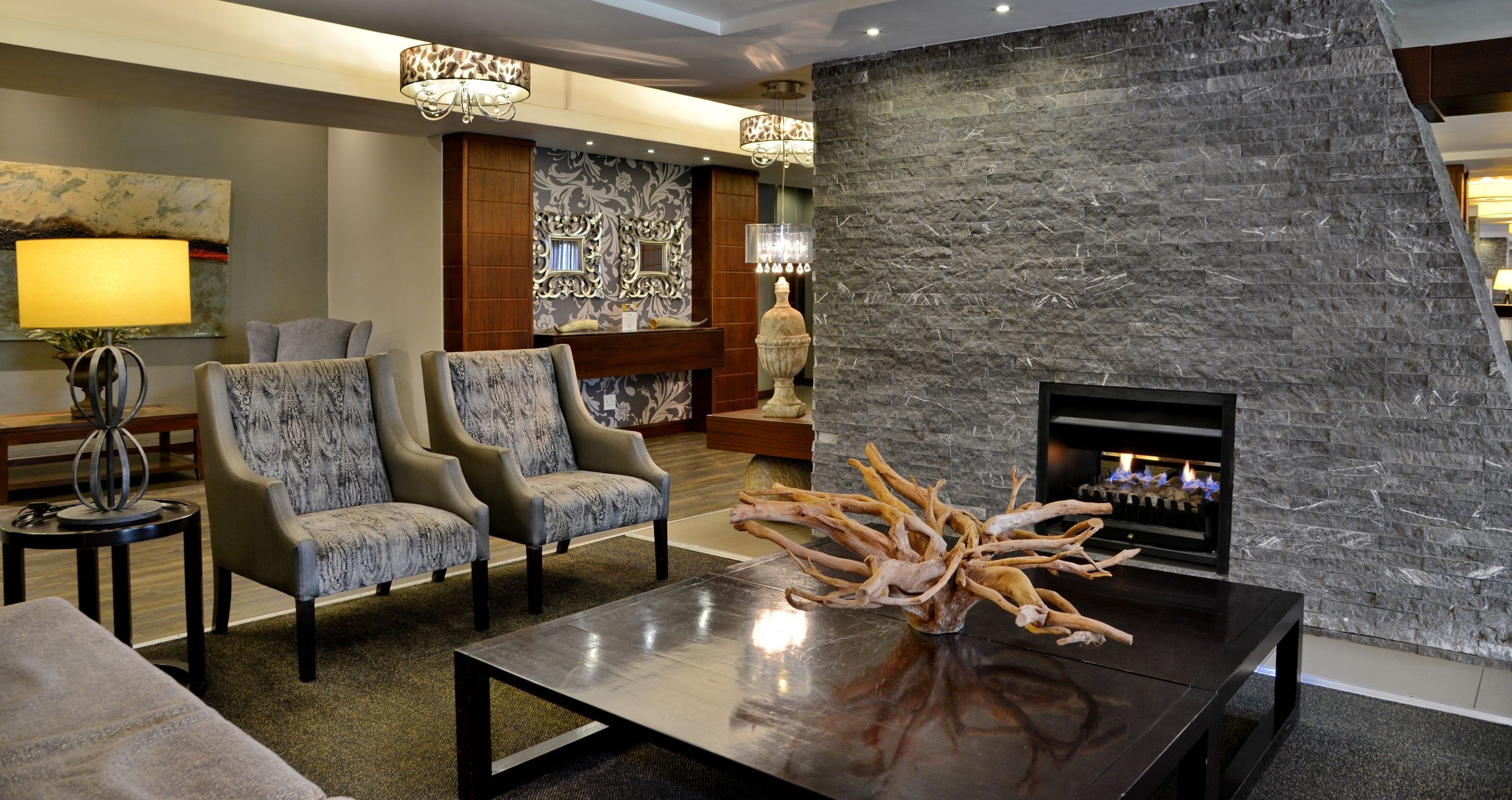 A modern lobby with two armchairs, a coffee table with a decorative centerpiece, a fireplace, and a stone accent wall.