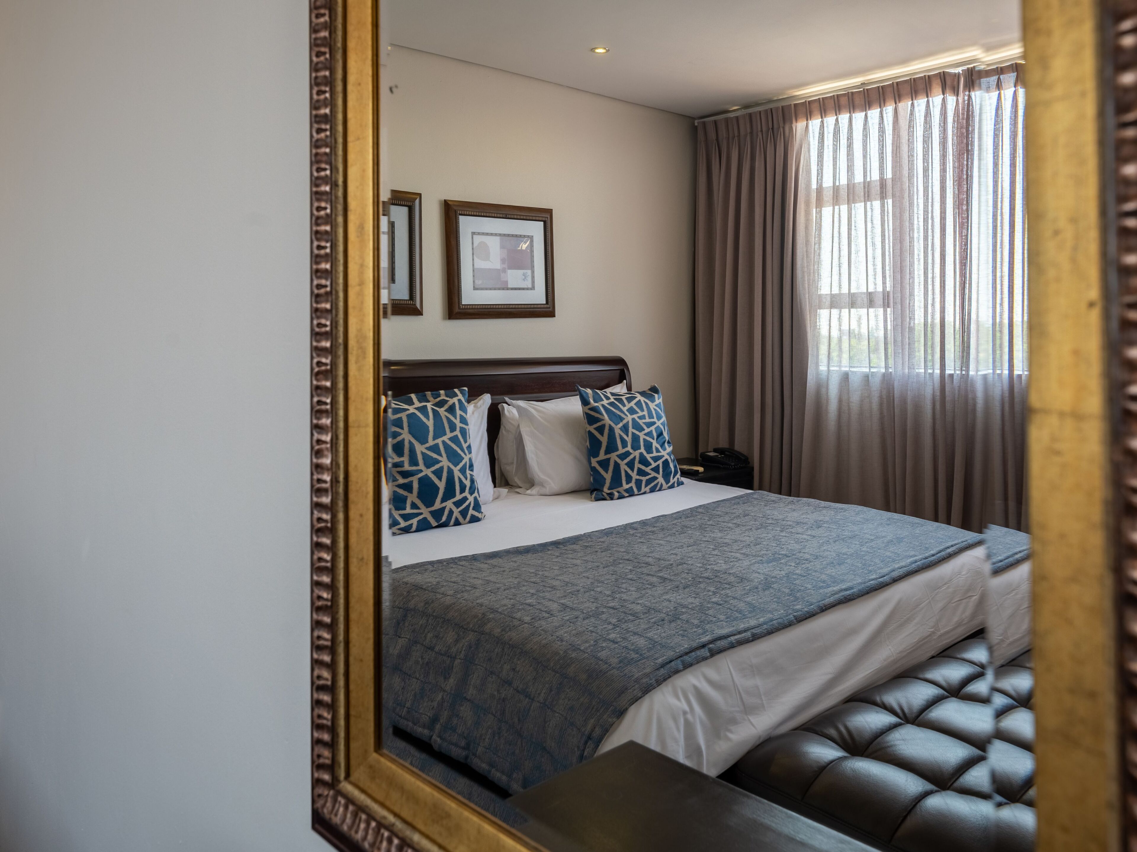 A neatly made bed with a headboard, two framed pictures on the wall, and a window with curtains.
