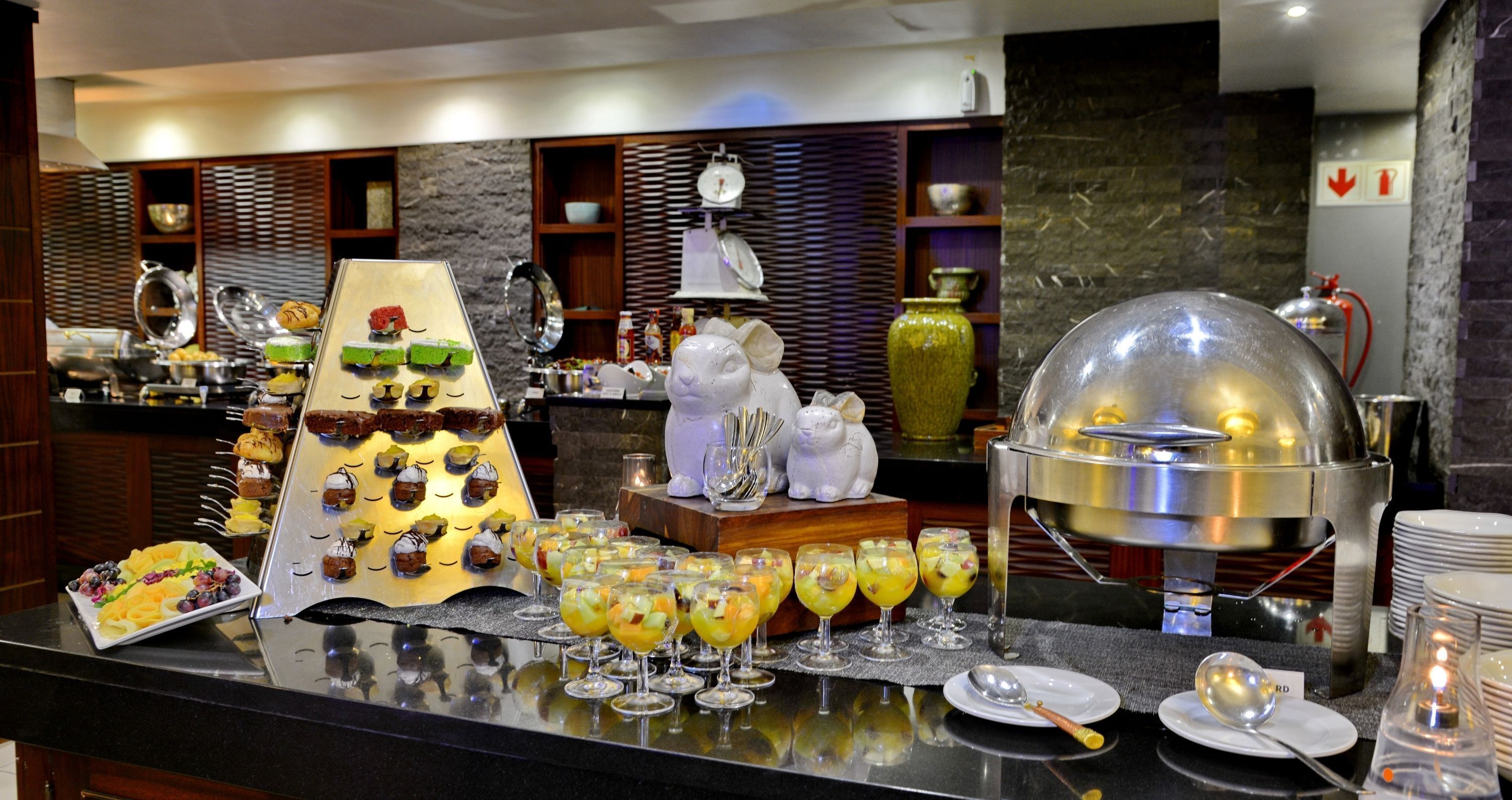A buffet setup with various food items and beverages, a decorative white rabbit statue, and a large metal dome cover over a buffet station.