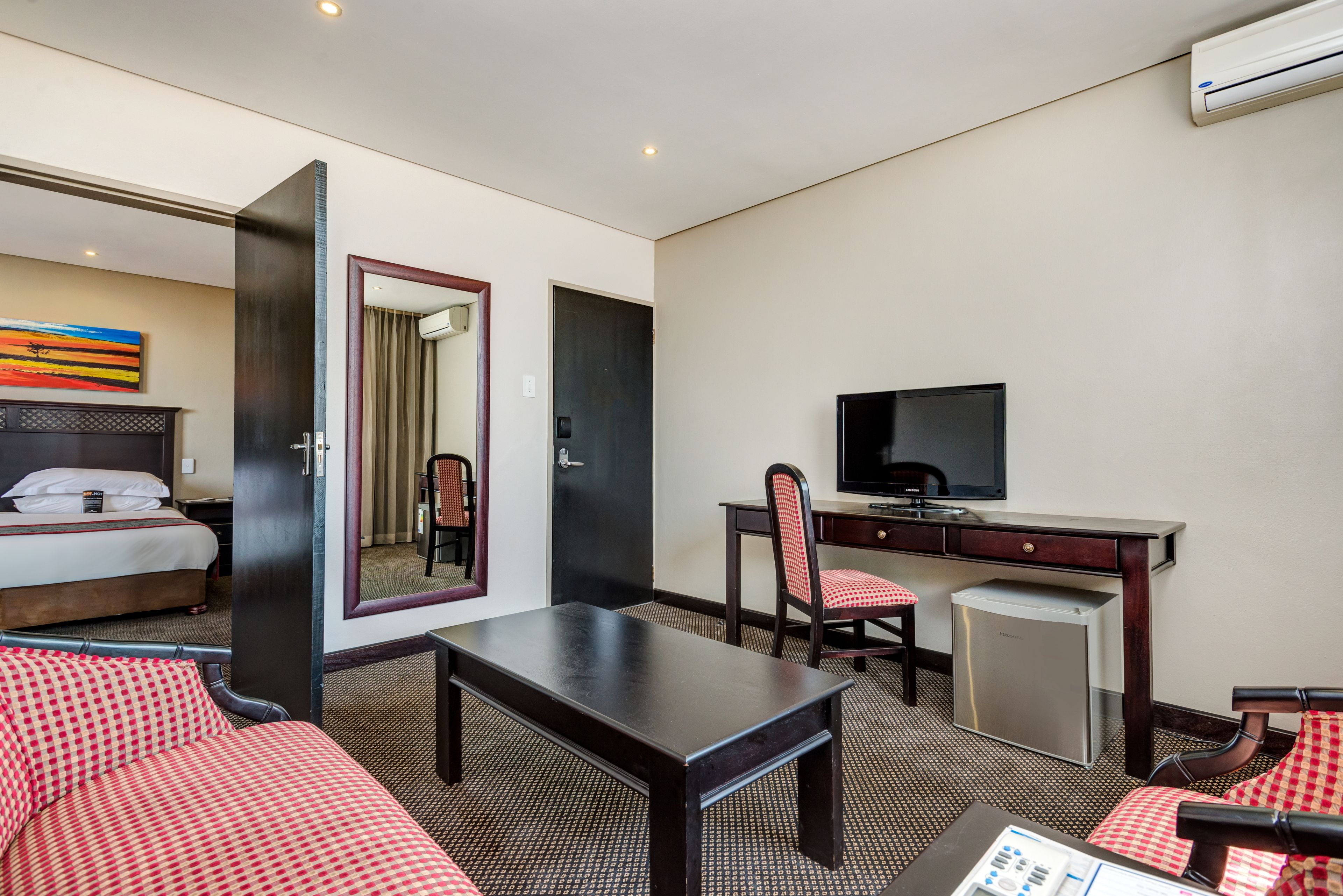 A hotel room with a bed, a desk with a chair, a television, and a small refrigerator.