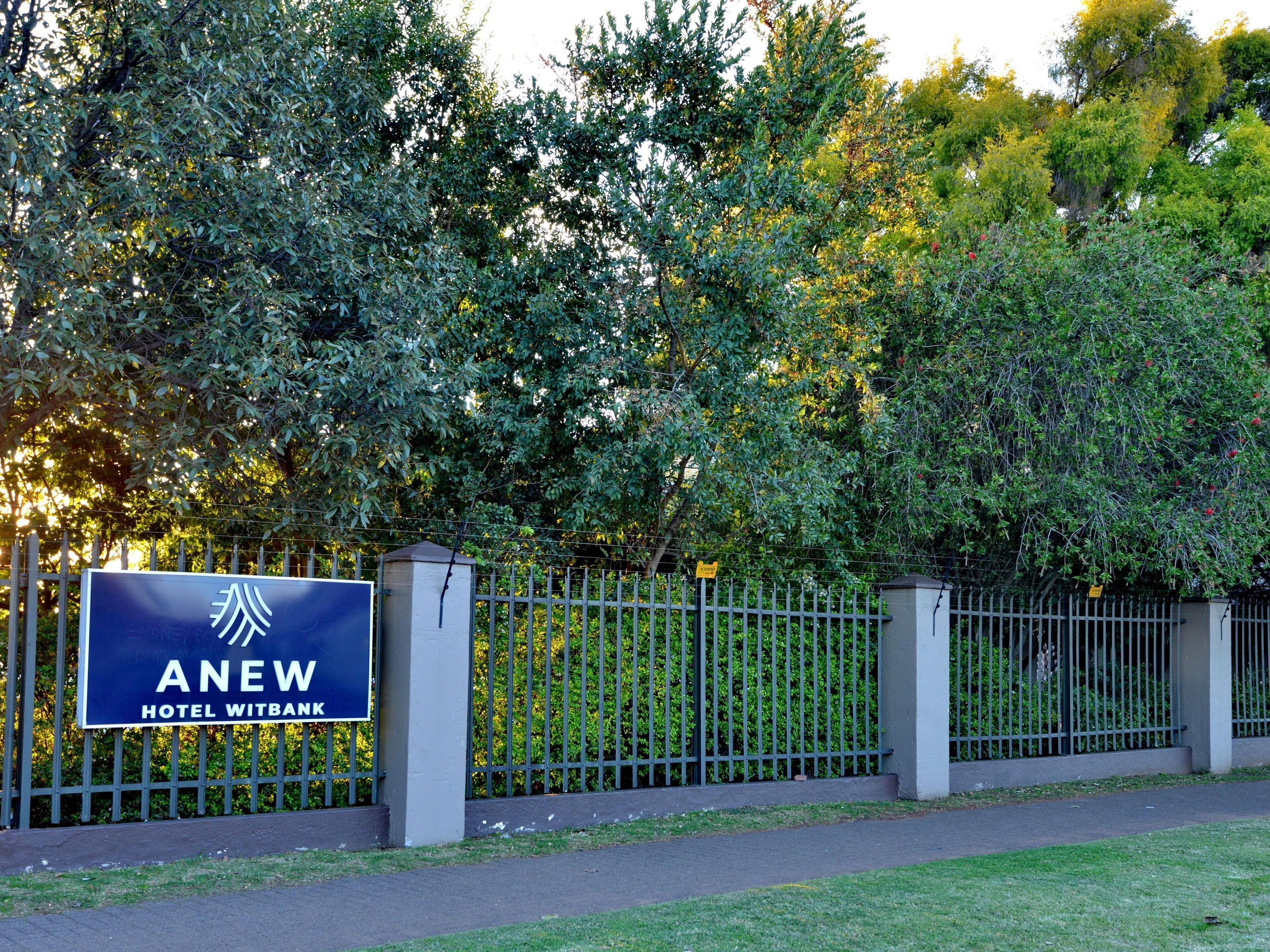 Letrero de hotel con el nombre 'ANEW HOTEL WITBANK' y una valla metálica.