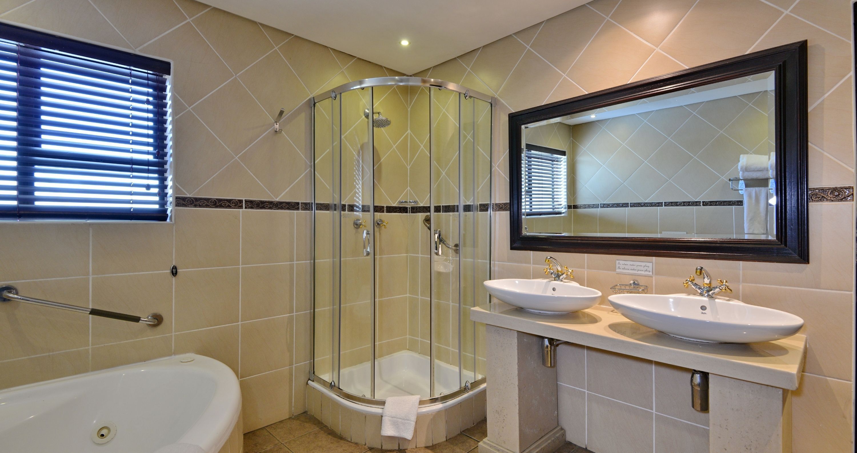 Un baño con ducha de mampara, dos lavamanos, una bañera y un espejo grande.