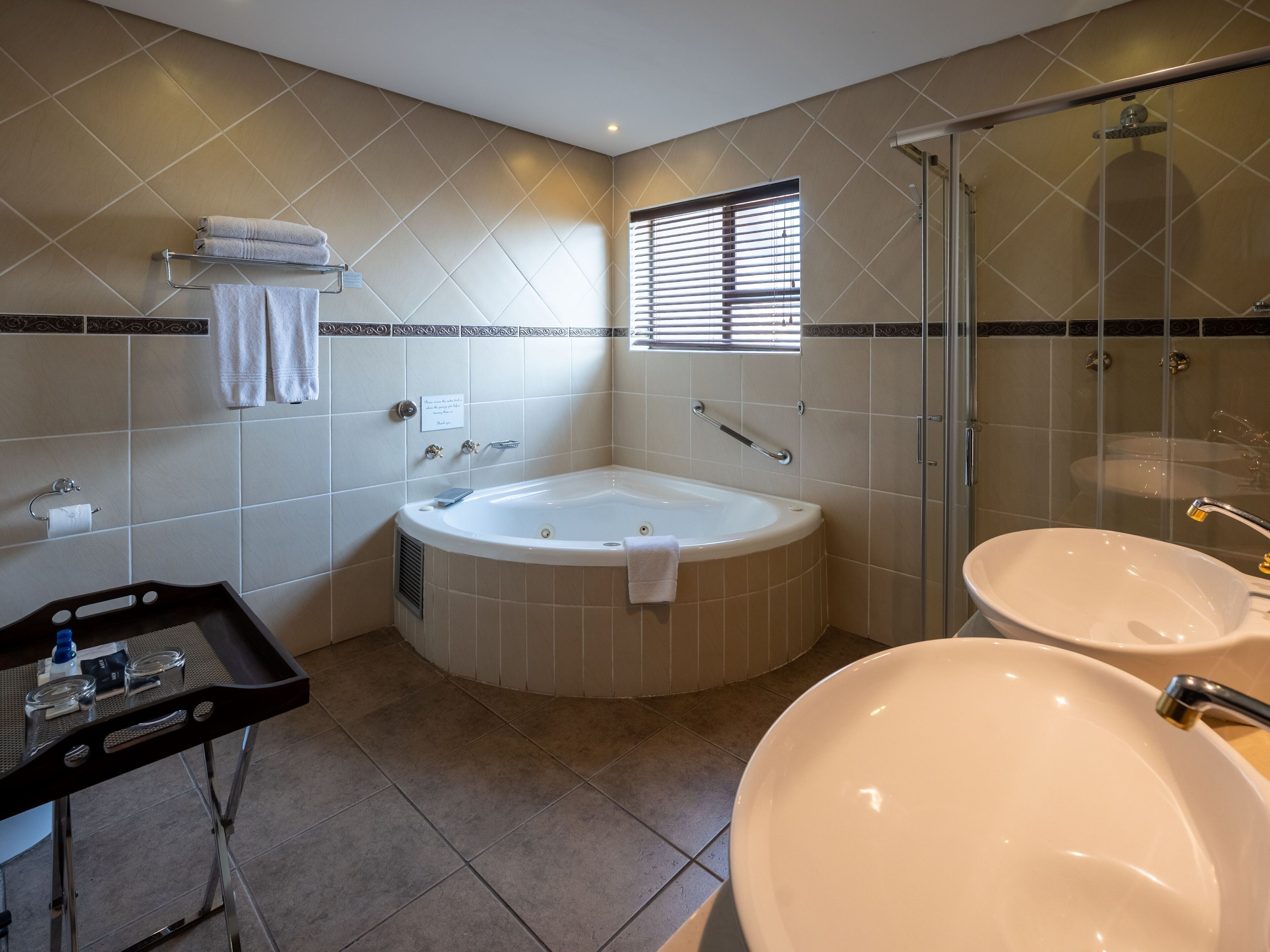 A modern bathroom with a bathtub, two sinks, a glass shower enclosure, and a vanity with a tray.