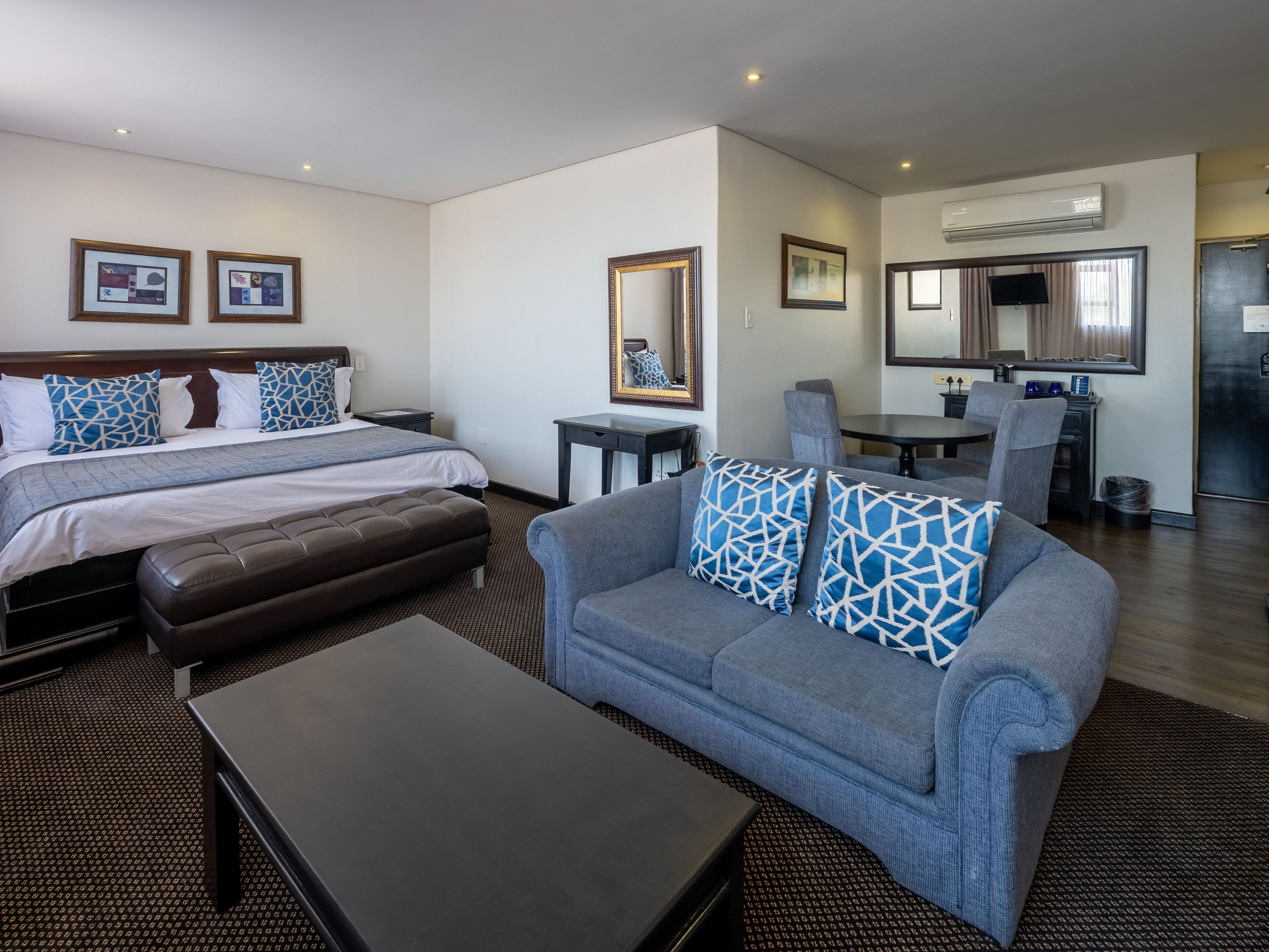 Habitación de hotel con dos camas, un sofá, una mesa de centro, un comedor y un televisor.