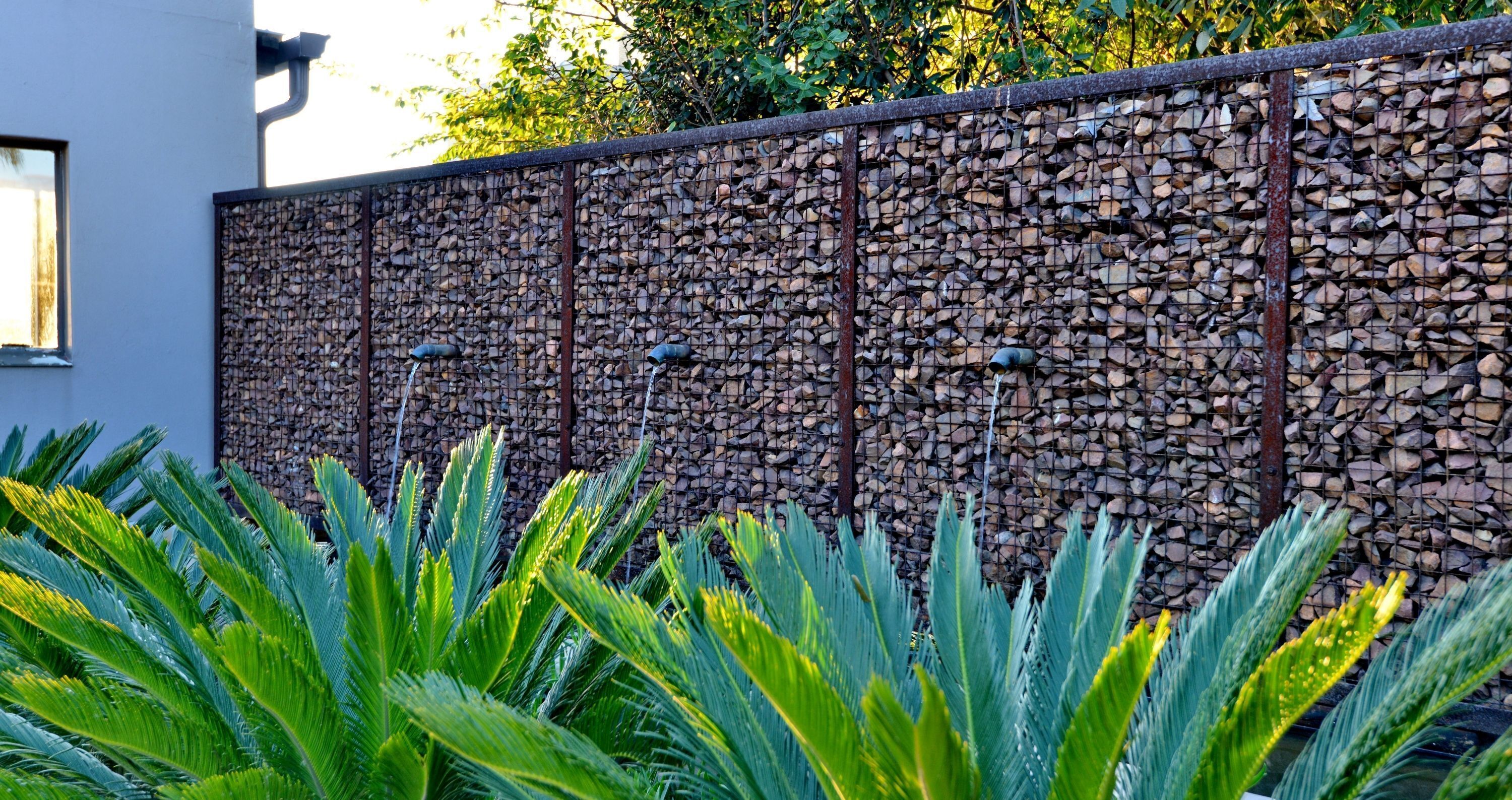 Una pared con textura de piedra y una valla metálica.