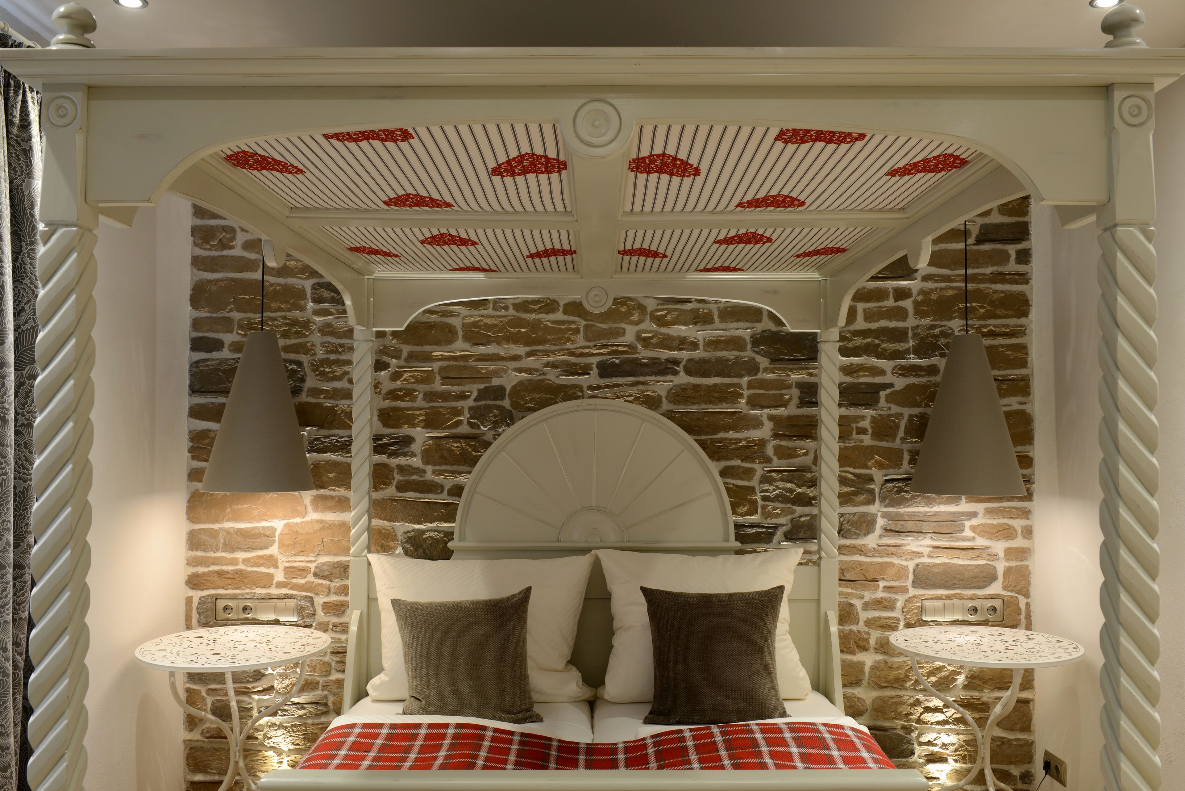 A cozy bedroom with a stone wall, a bed with a white headboard, and two bedside tables with lamps.