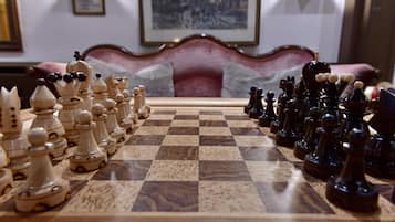 Taula de joc d'escacs preparada en una habitació amb una cadira antiga i quadres emmarcats a la paret.